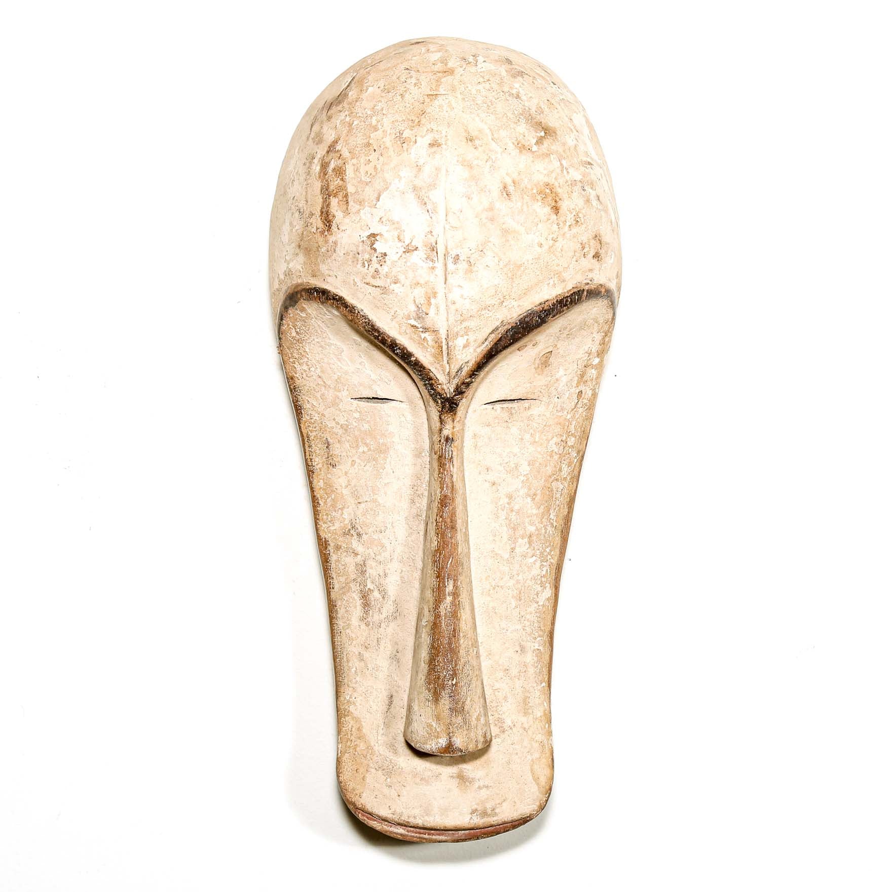 Decorative white African Fang tribe carved wood mask resembling a stylized face on a white background