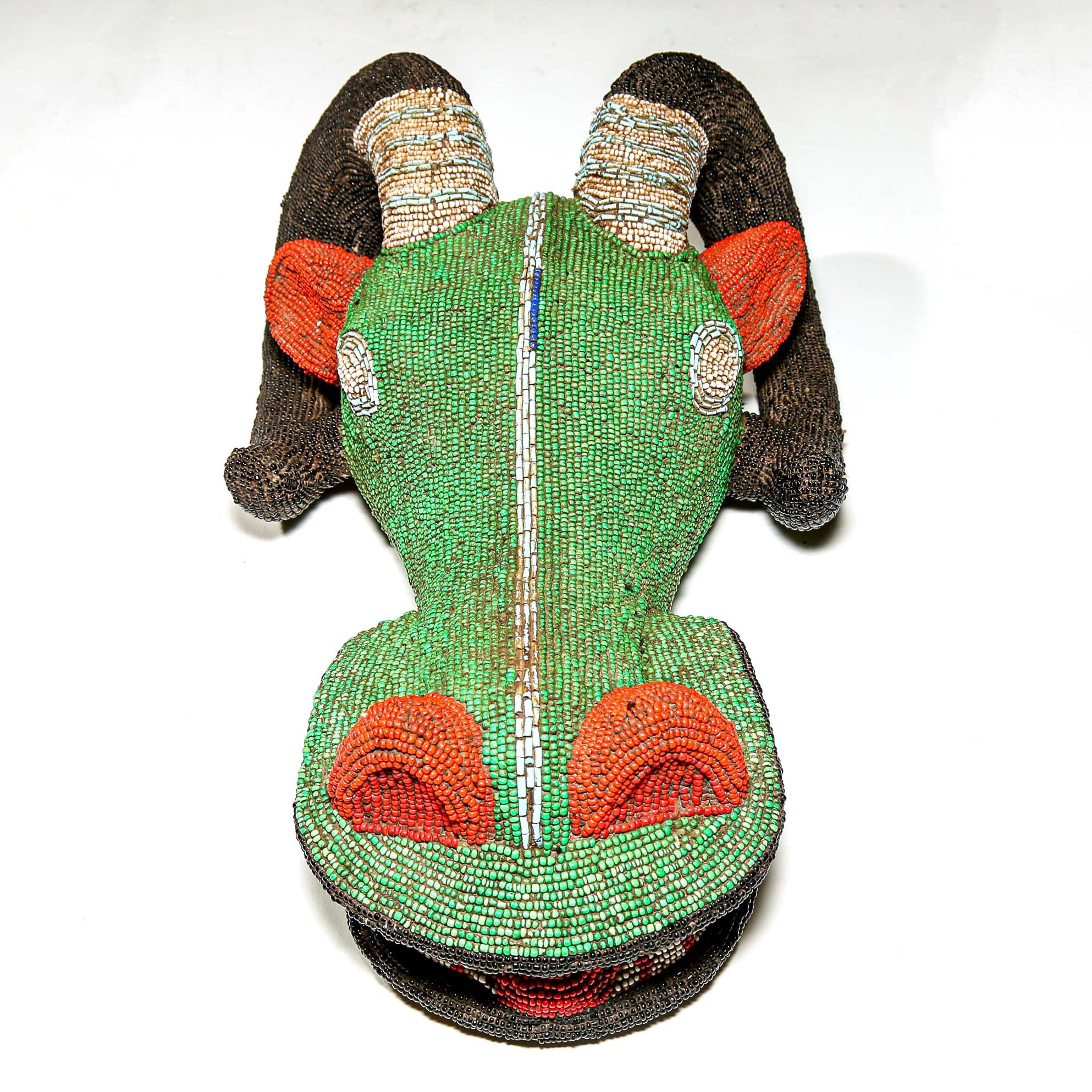 Decorative African object with green beadwork, brown and red accents on a white background