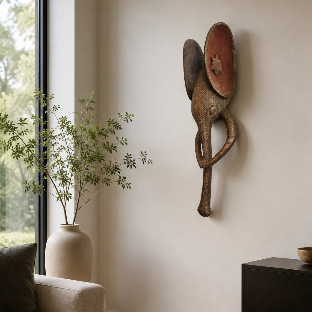 Decorative wall sculpture on a neutral wall with a vase and plant in the foreground.