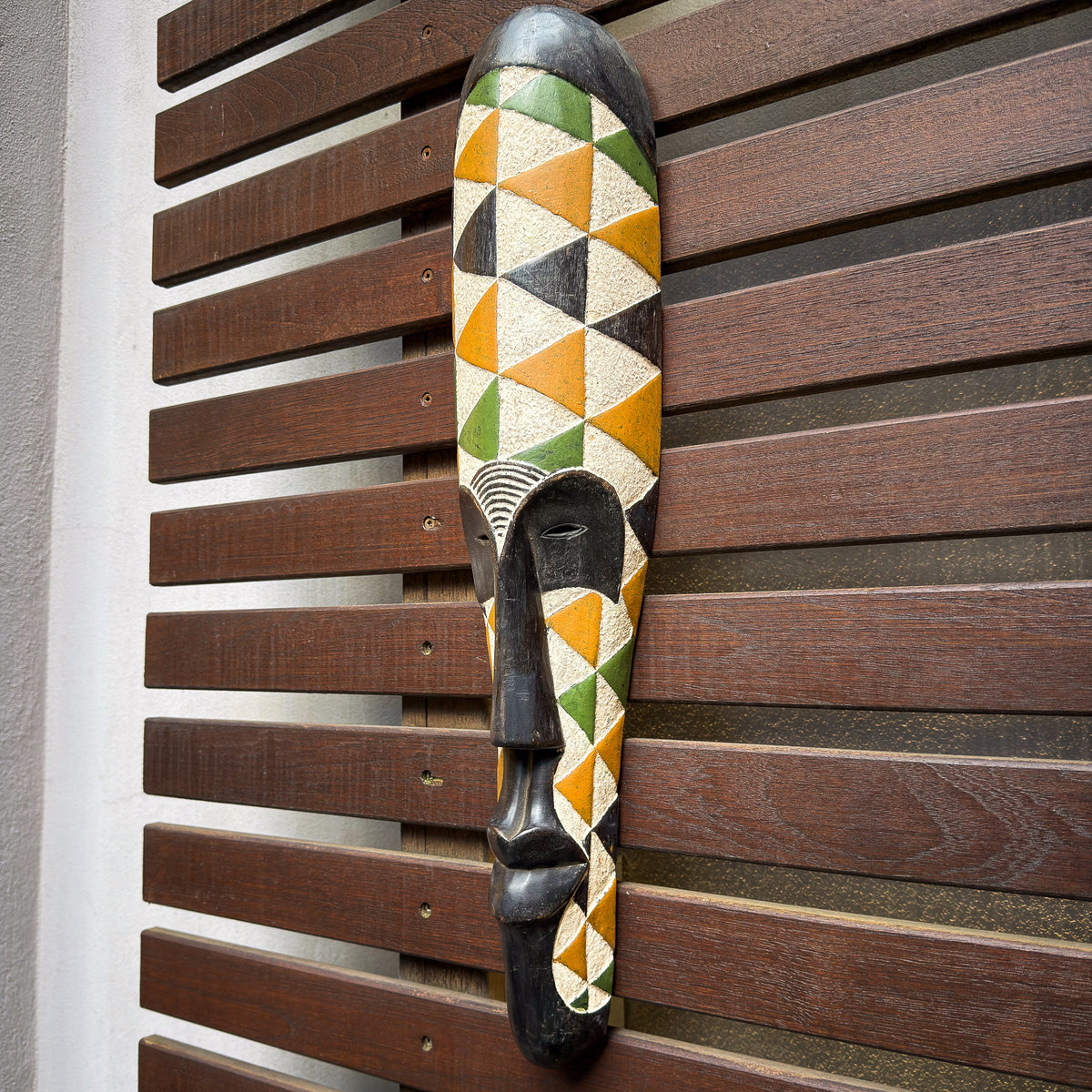 Colorful African face mask inspired by Fang traditions with painted surface patterns and distinctive elongated proportions
