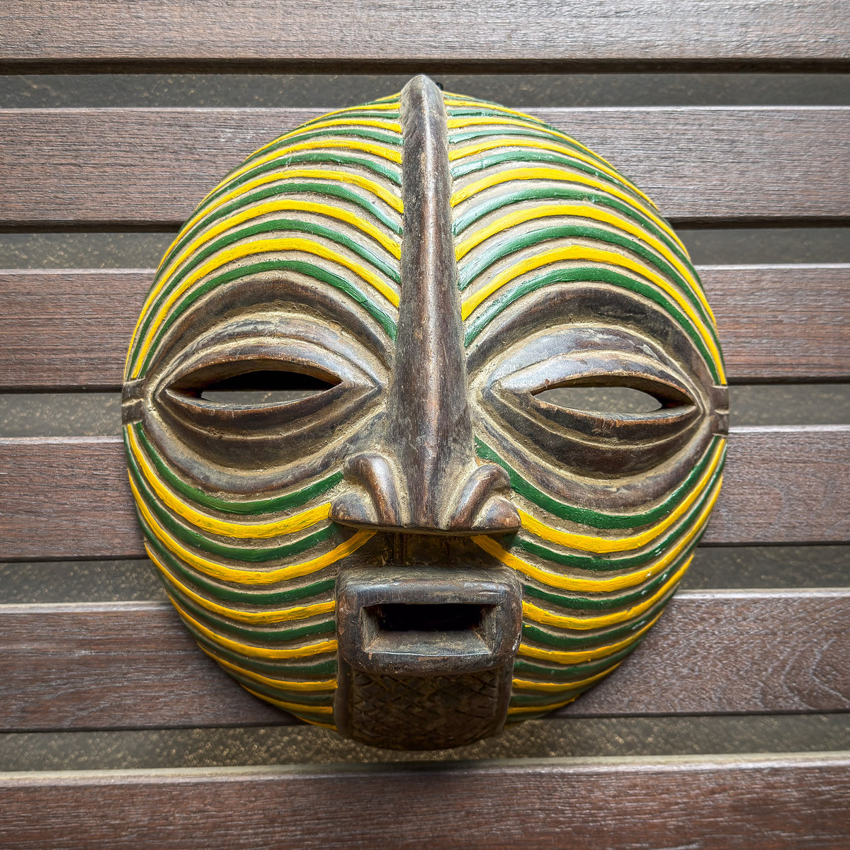 Round Songye Kifwebe mask from the Democratic Republic of Congo with bold yellow and green striped decoration