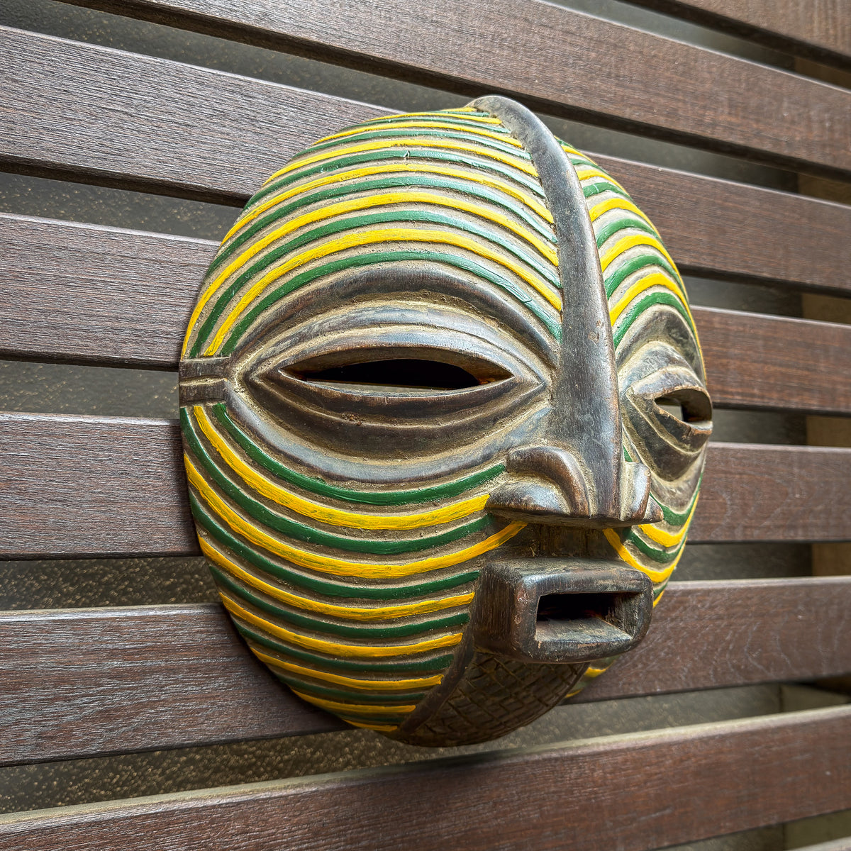 Yellow and green Songye mask featuring a circular form, graphic painted stripes, and distinctive Central African styling