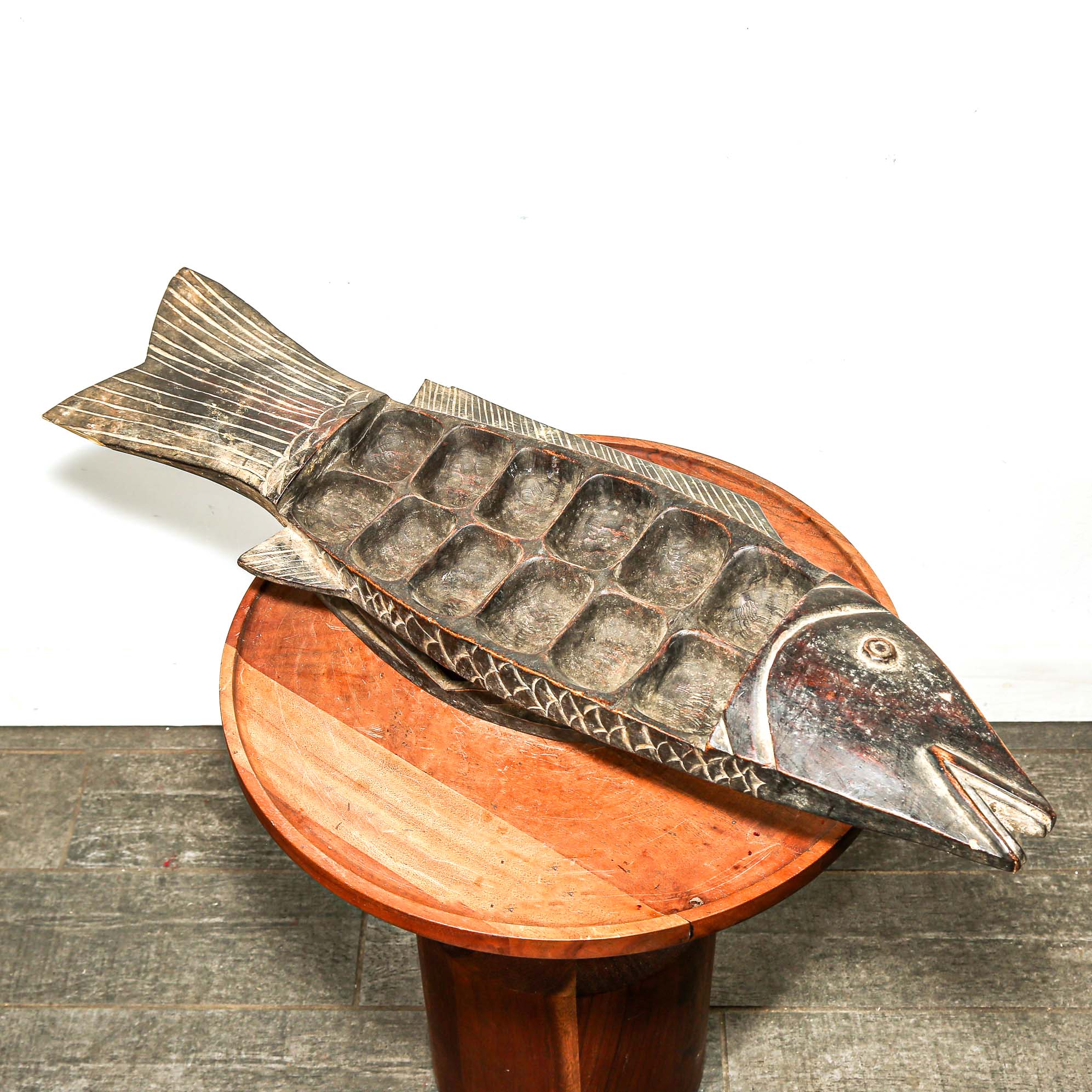 Wooden fish-shaped cutting board on a wooden stand with a white background