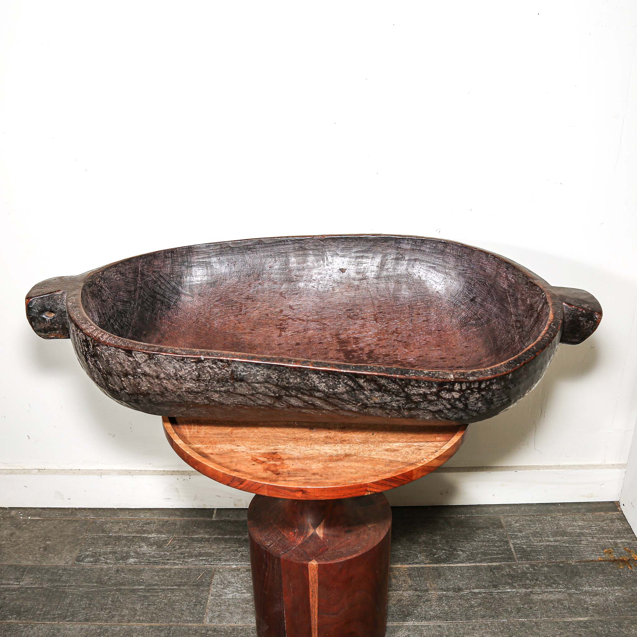 Decorative wooden vintage African oval bowl on a stand against a white wall