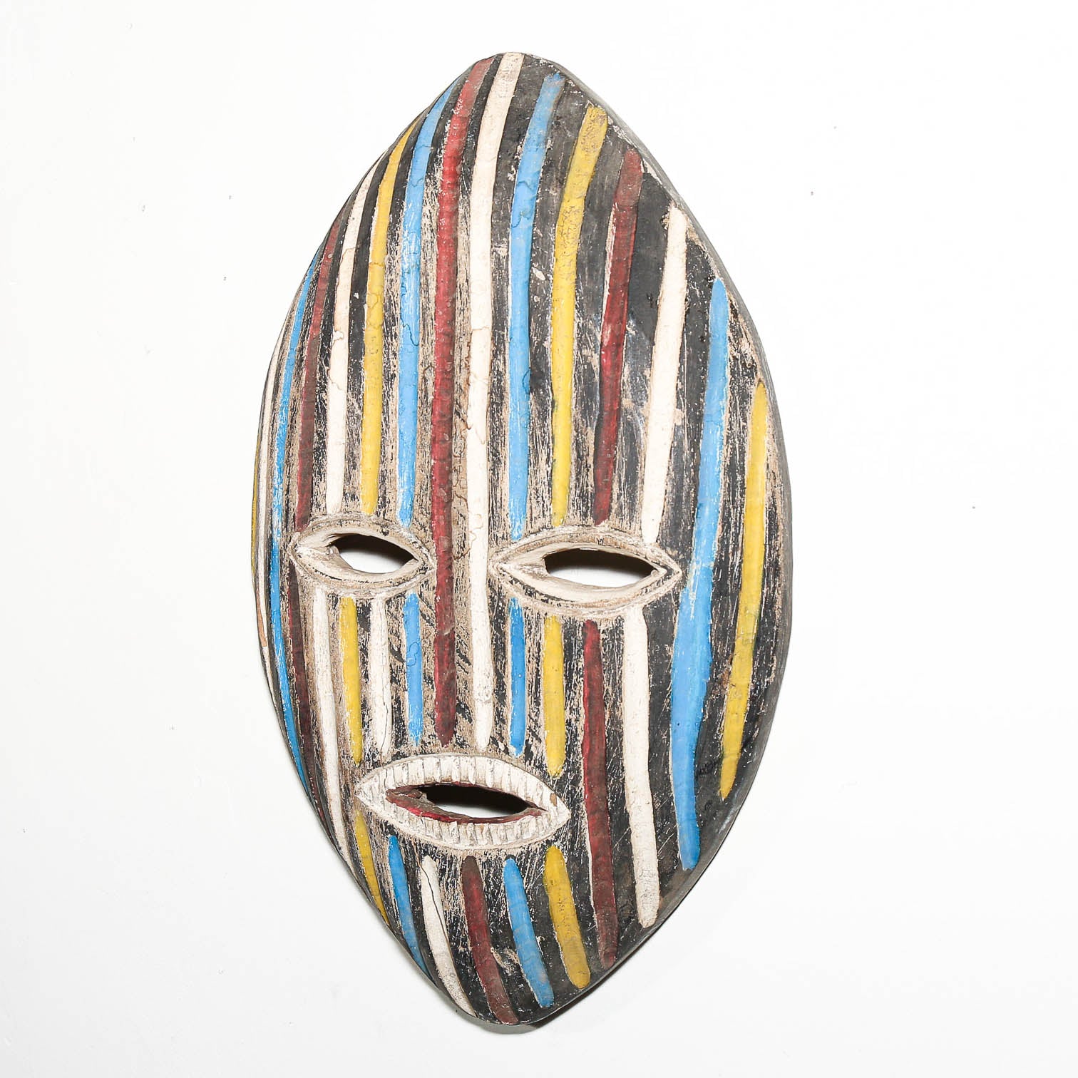 A hand-painted wooden mask with a vertical striped pattern in blue, yellow, red, white, and black, featuring cutouts for the eyes and mouth, shown against a plain white background.