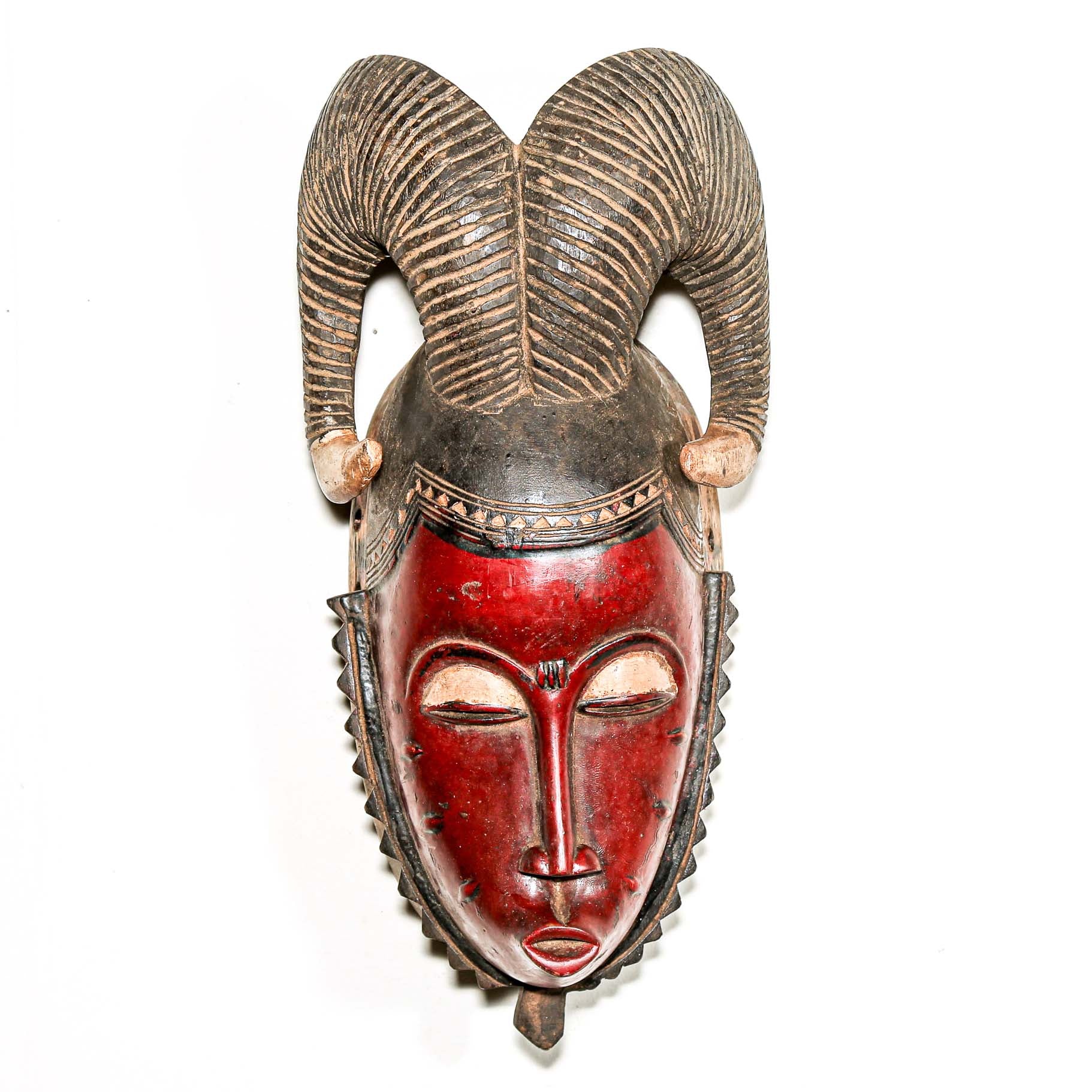 Hand-made African mask with red face and decorative horns on a white wall