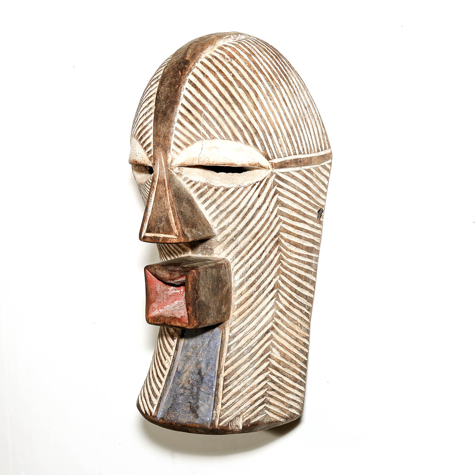 A carved wooden African-style mask with geometric facial features, hand-painted brown and blue accents, and a textured finish, shown against a plain white background.