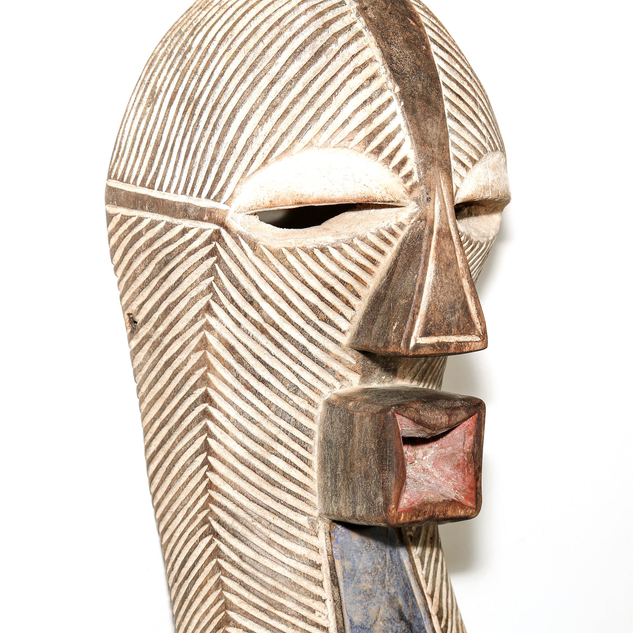 A carved wooden African-style mask with geometric facial features, hand-painted beige and brown tones, and a reddish-brown mouth cavity, shown against a plain white background.