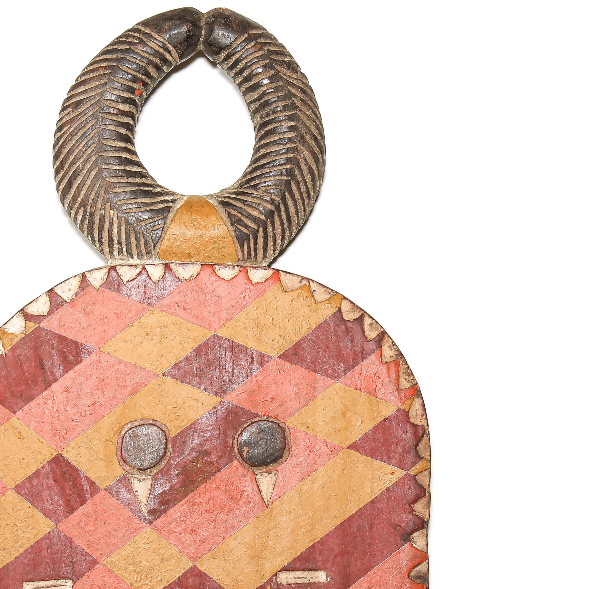 A close-up of a handcrafted wooden decorative African object with a large loop handle and a geometric patterned face, shown against a plain white background.