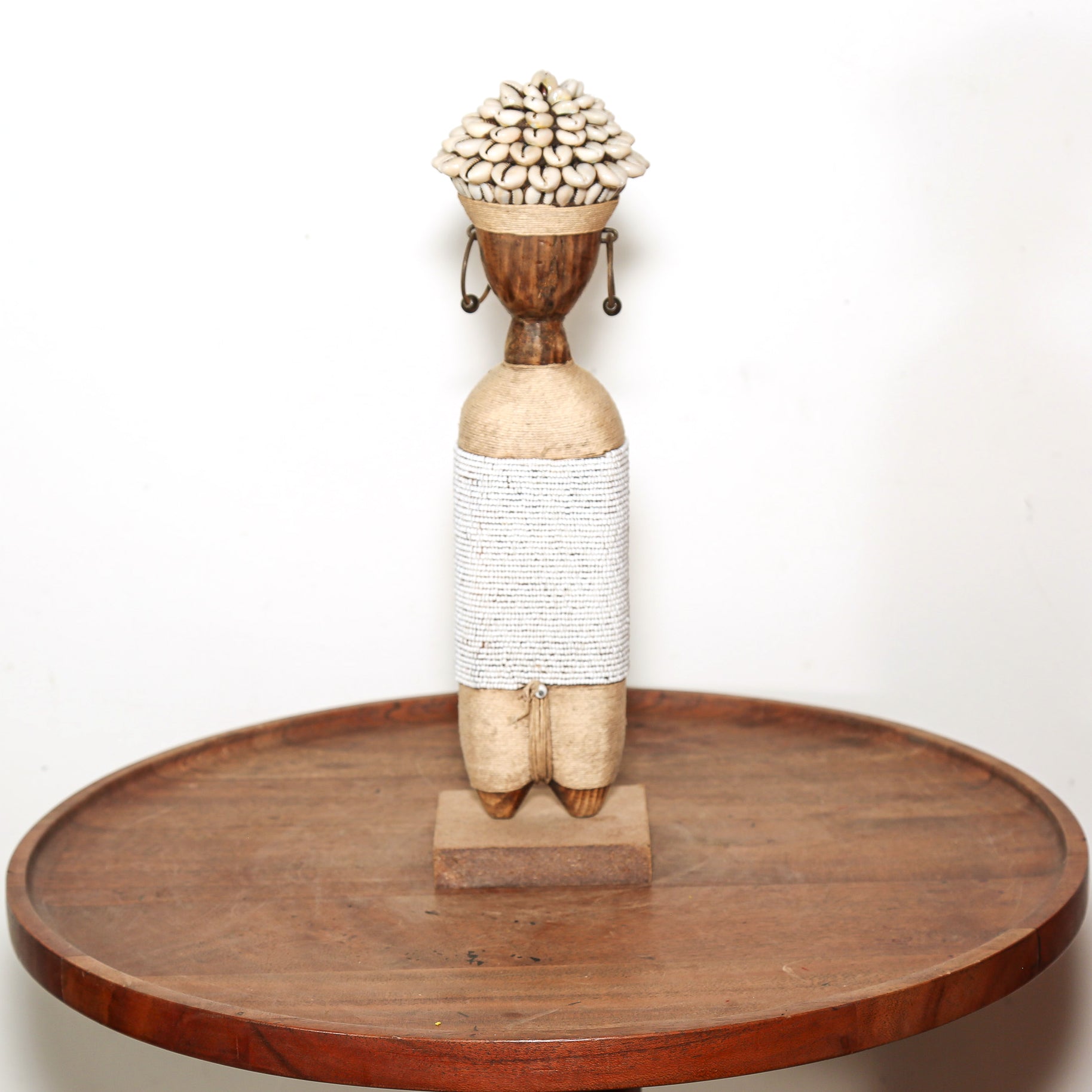 A handmade African-style wooden doll sculpture standing on a round wooden tray against a plain white background.