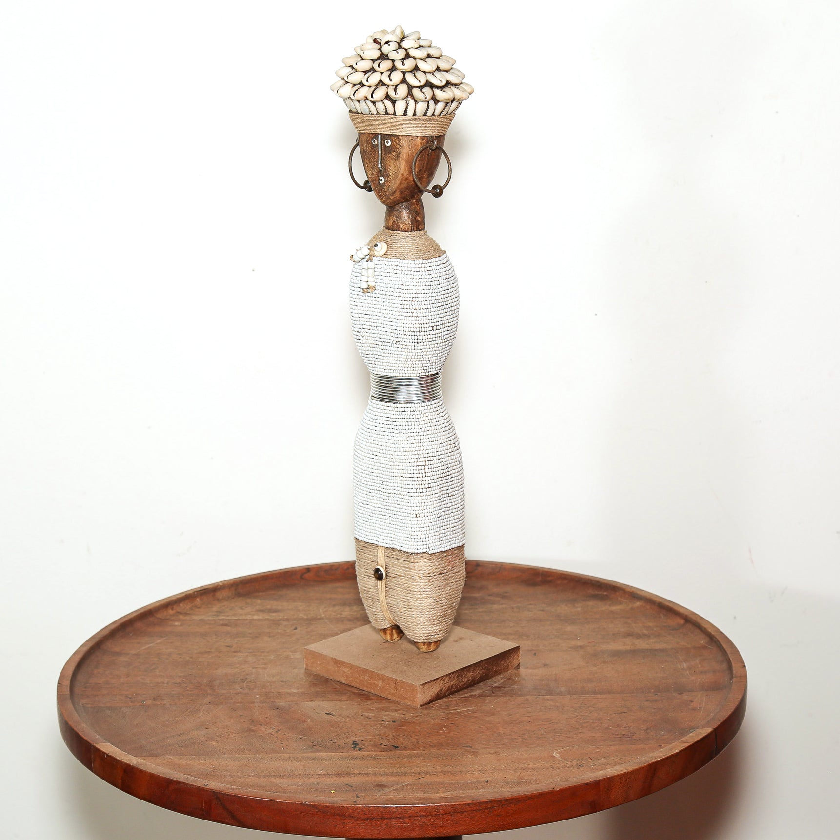 A decorative African-style wooden figurine sculpture displayed on a round wooden table against a plain white background.
