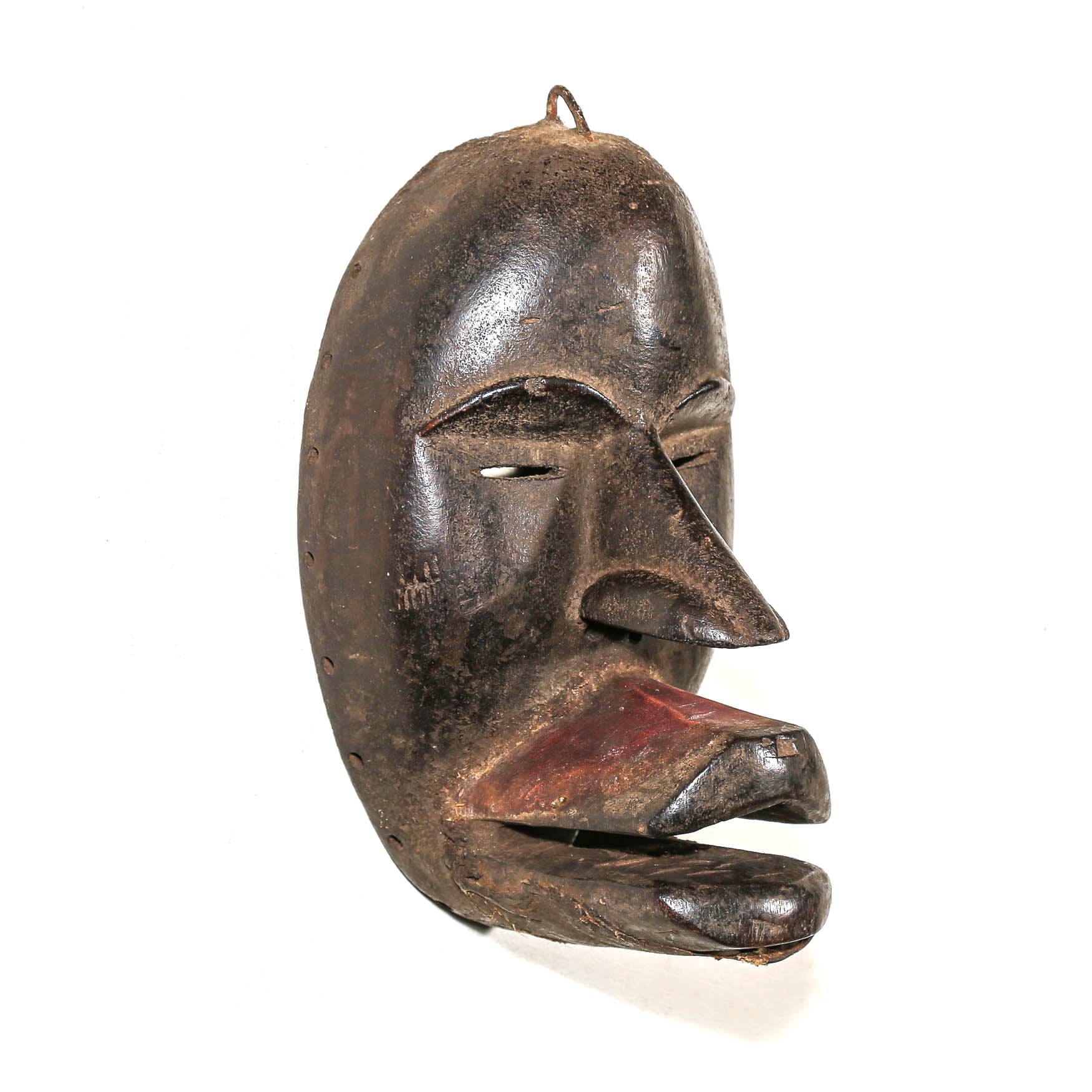 A black carved wooden mask with a crescent moon shape, featuring a weathered brown finish and a reddish-brown painted interior around the mouth area, shown against a plain white background.