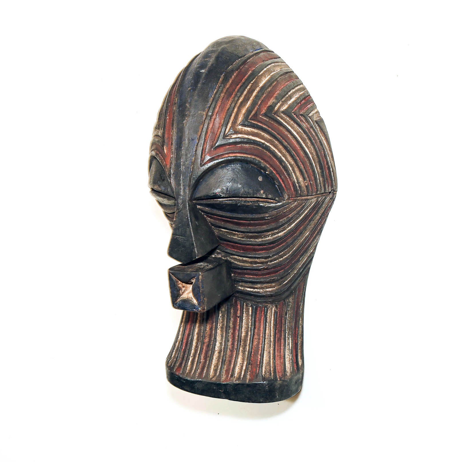 A carved African-style mask with a dark black base and intricate red, brown, and beige striped geometric patterns, shown on a plain white background.