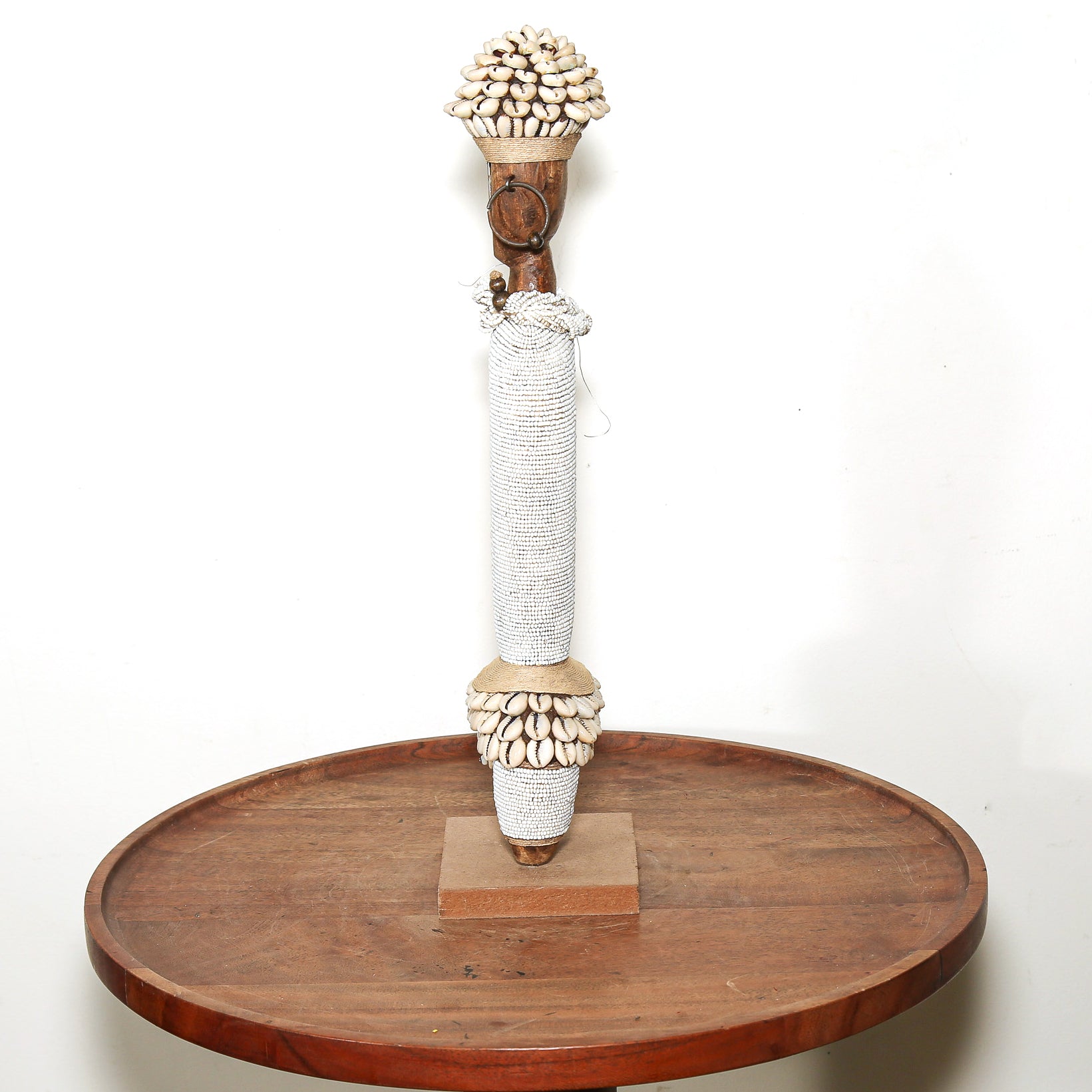 A decorative wooden and shell doll stand with a wrapped central shaft, displayed on a round wooden tray against a plain white background.