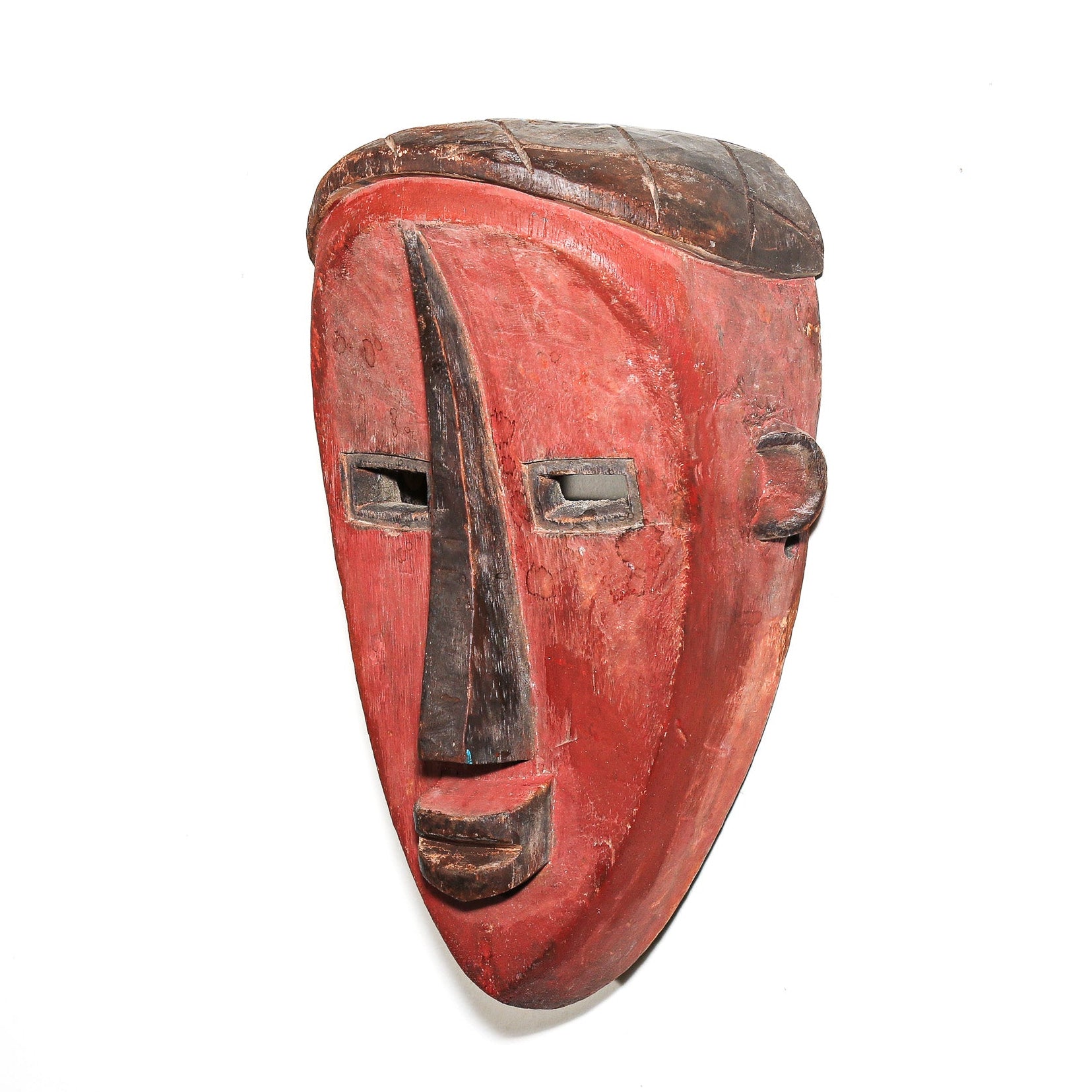 A hand-carved wooden mask with a red-painted face and dark brown details, shown against a plain white background.