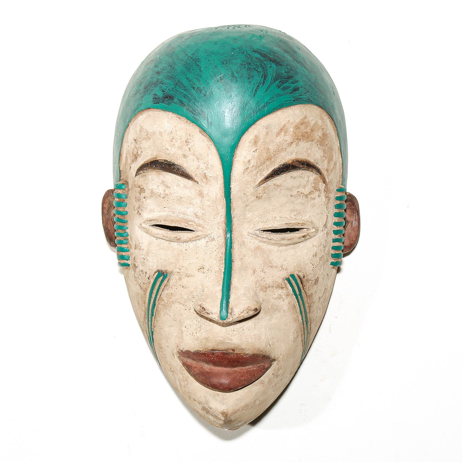 A hand-carved African wooden mask with a painted teal green top and cheeks, a beige face, and brown lips, shown against a plain white background.