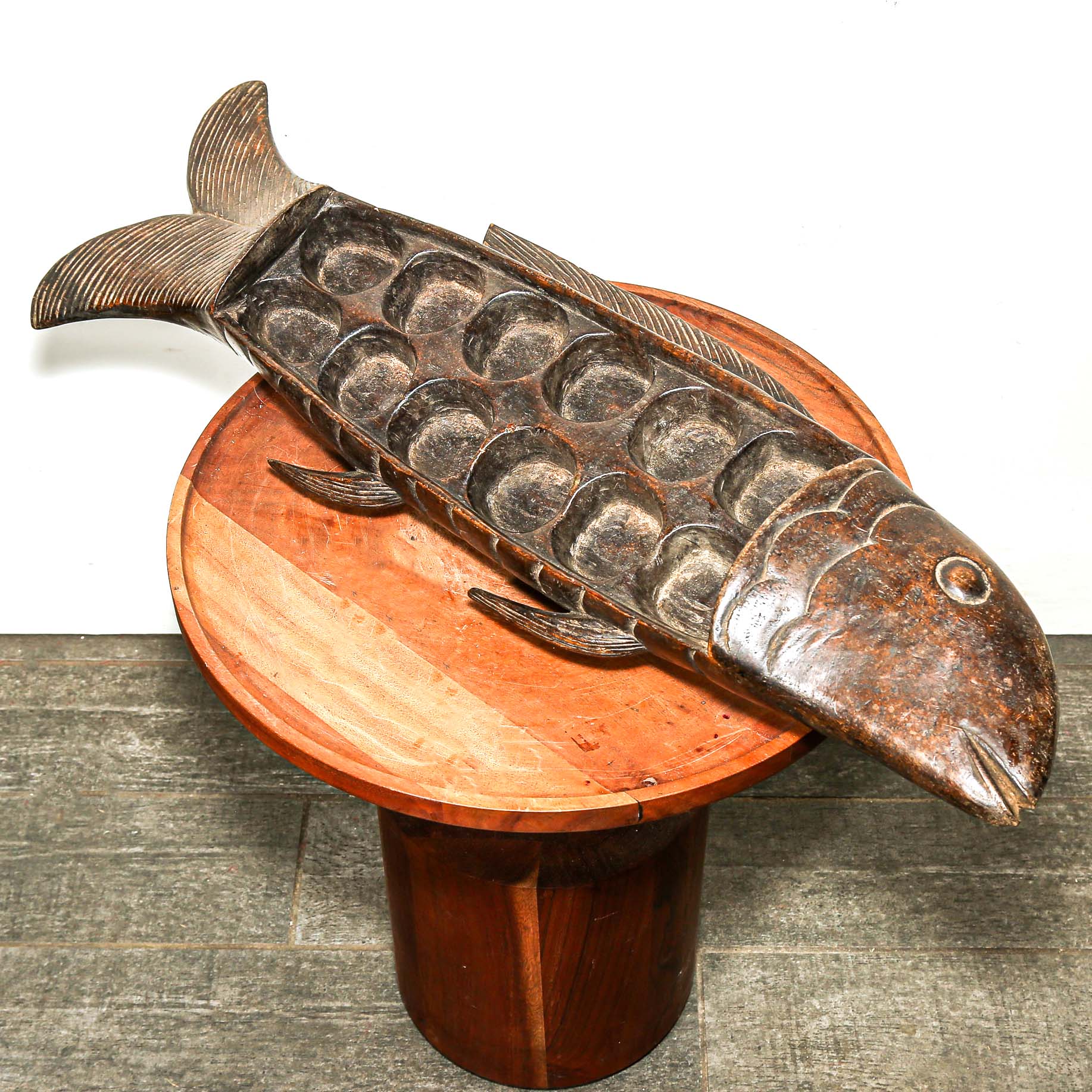 Wooden fish sculpture on a wooden pedestal against a white background
