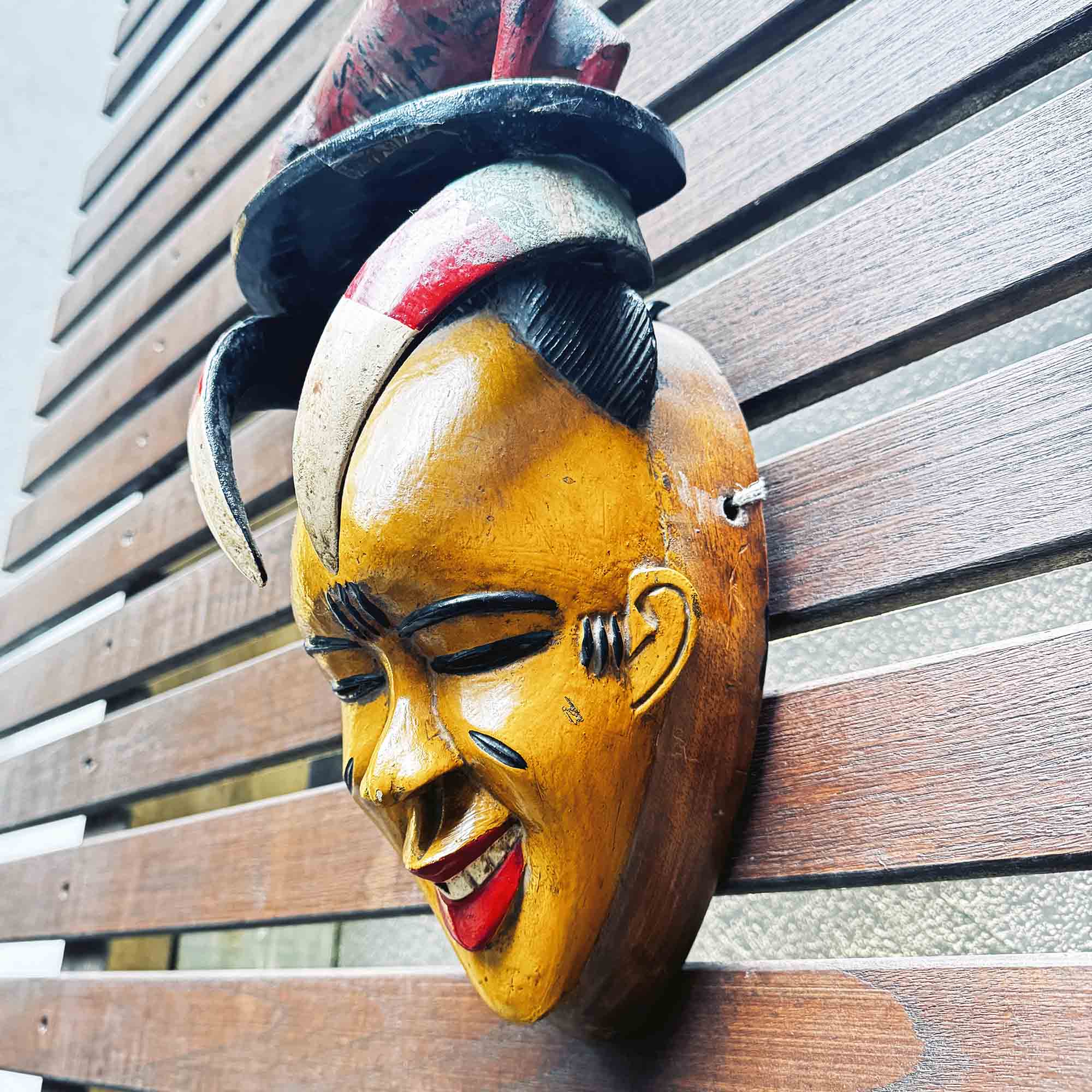 Wooden mask with yellow face and red lips on a wooden surface