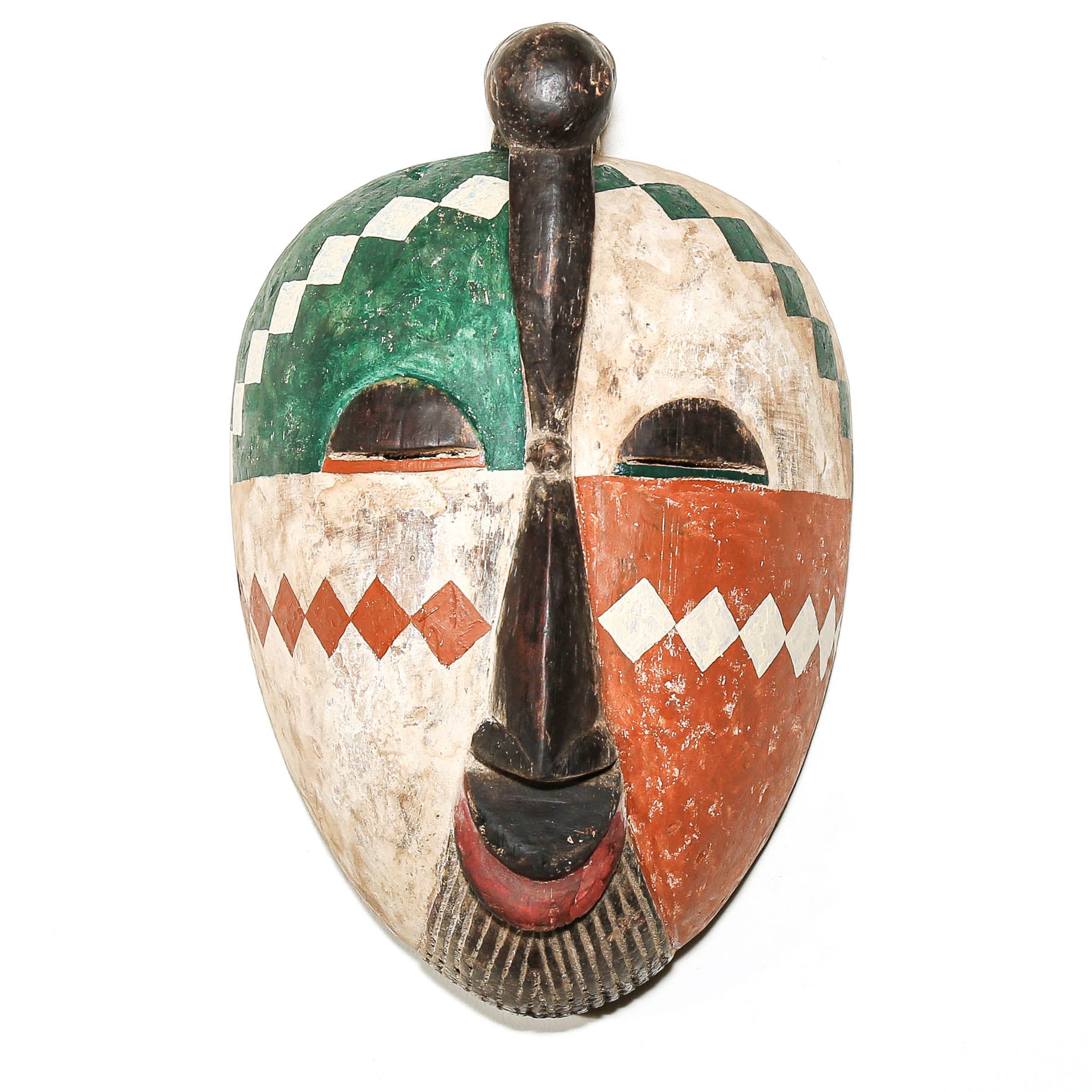 A hand-painted wooden African-style mask with a vertical split design, featuring green and white checkered patterns on the top, orange and white diamond patterns on the cheeks, and a dark central vertical feature, shown against a plain white background.