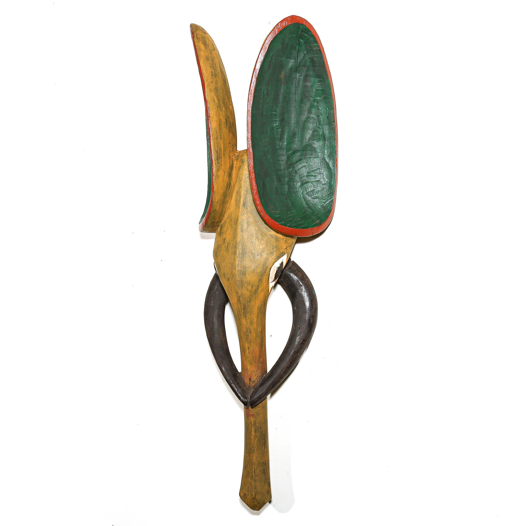 A hand-carved wooden wall hanging sculpture featuring a stylized figure with a green shield, red trim, and dark brown curved horns on a plain white background.