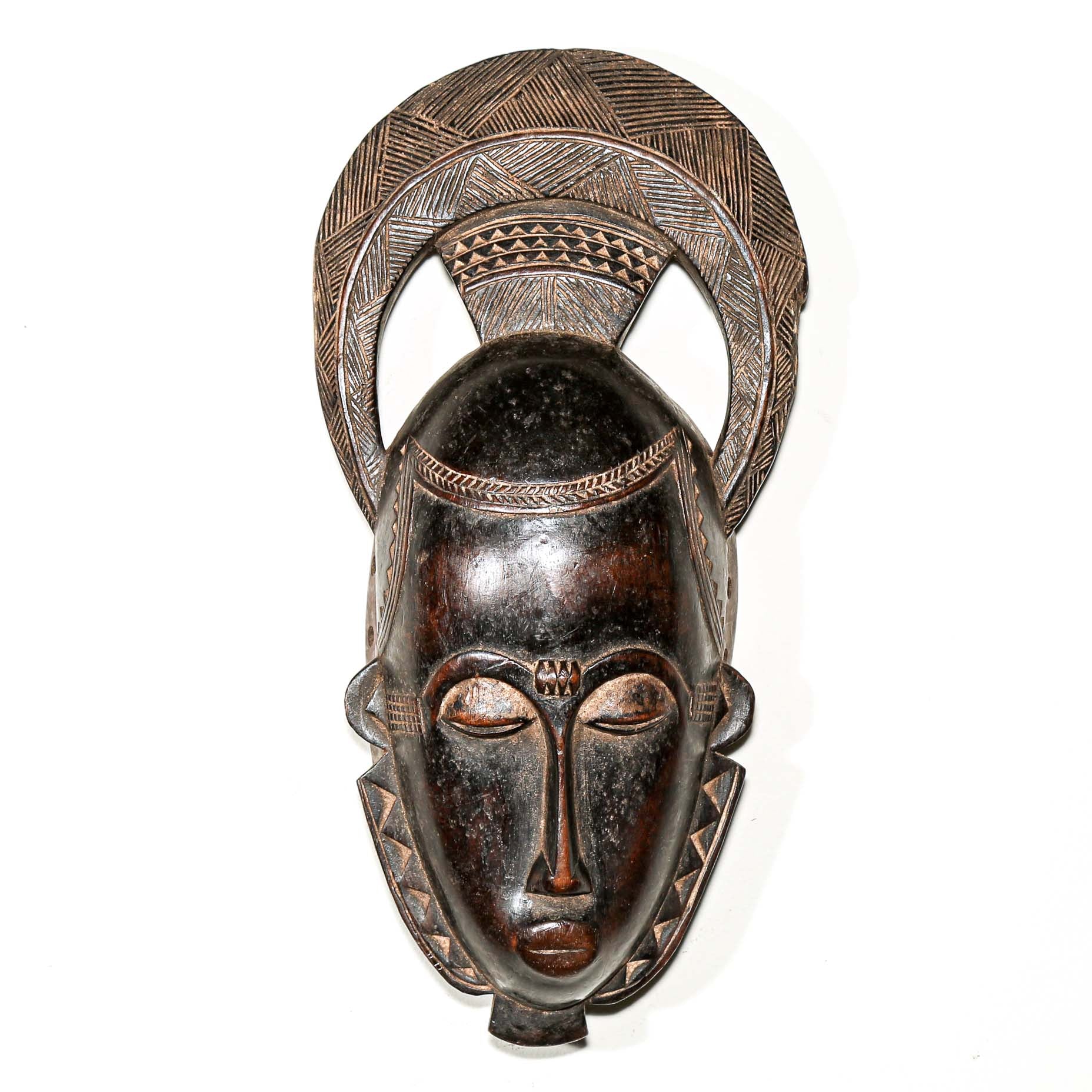 Finely carved wooden hand made african mask with intricate carvings on a white living room wall