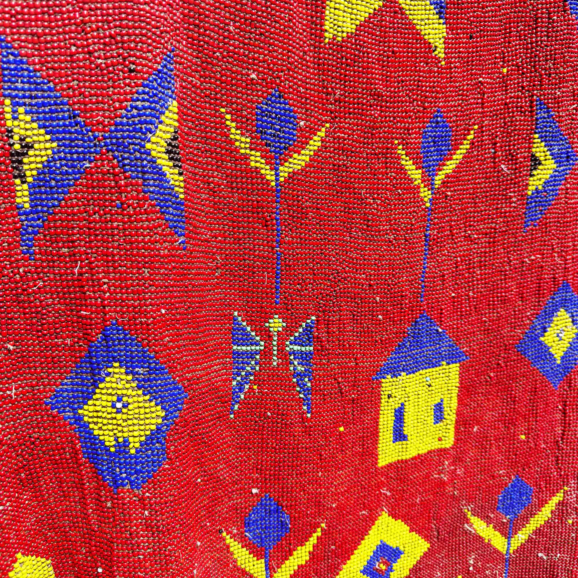 Close-up of a red fabric made from African beads with blue and yellow geometric patterns