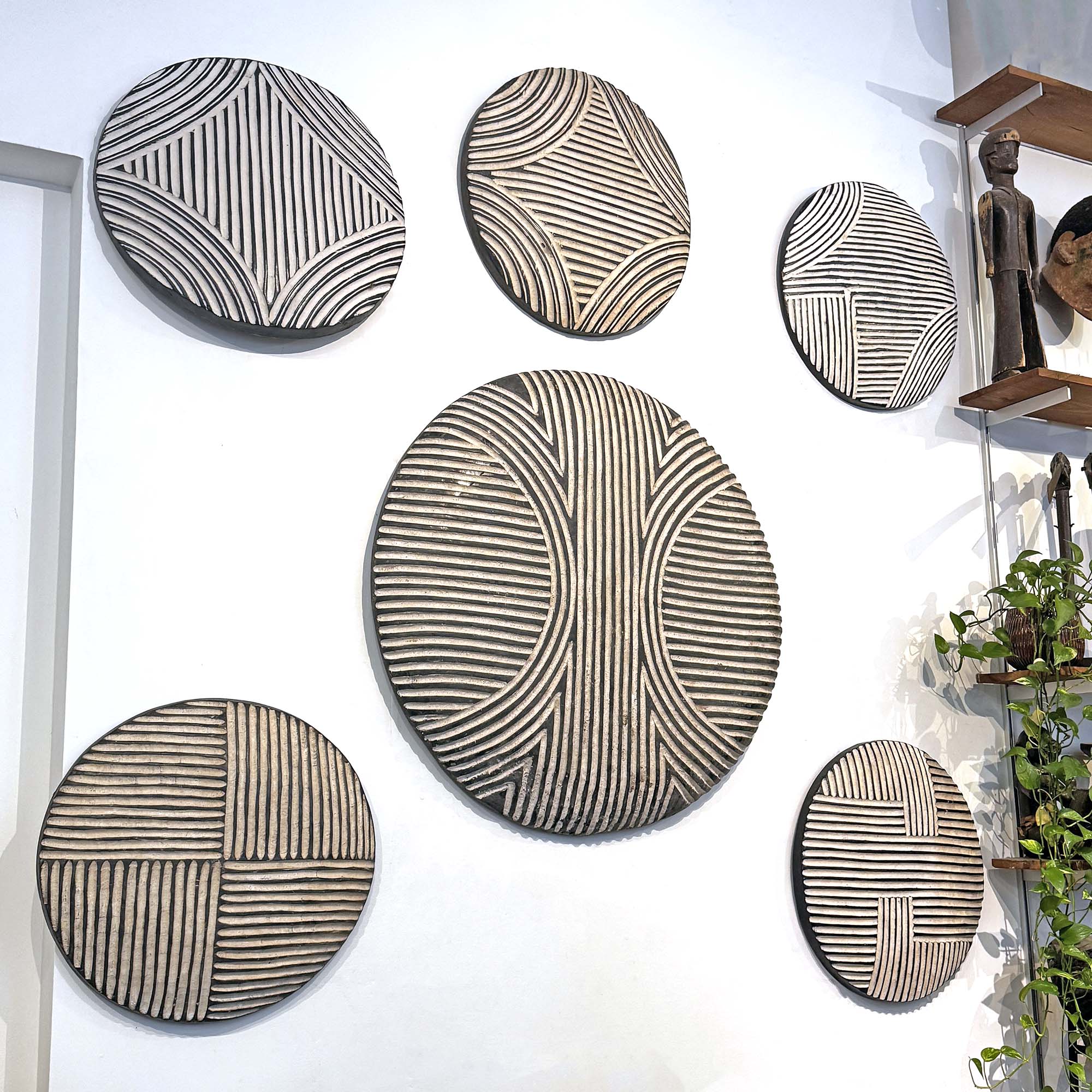 Set of six round wood African shields with geometric patterns on a white wall.