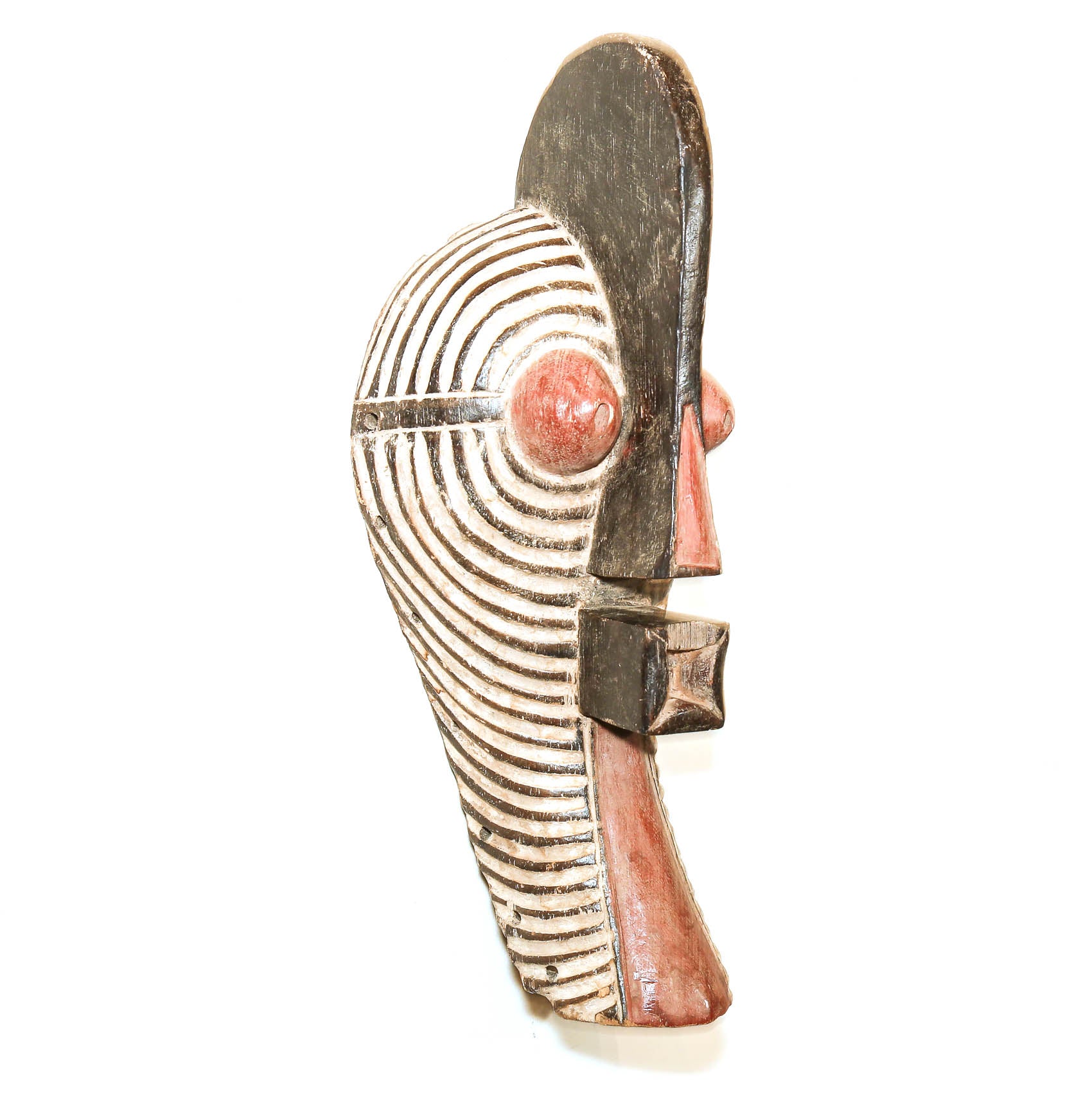 A hand-carved African wooden mask shown in profile against a plain white background. The mask features a dark brown wood body with hand-painted terracotta red details for the eyes, nose, and chin, and white painted accents highlighting the concentric curved lines on the head.