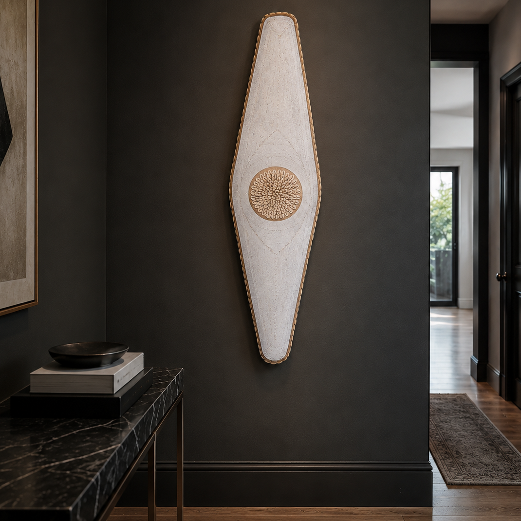 A large, vertically oriented abstract wall art piece with a textured off-white fabric body, gold-toned stitched border, and a circular woven gold center, mounted on a dark charcoal wall in a modern hallway setting.