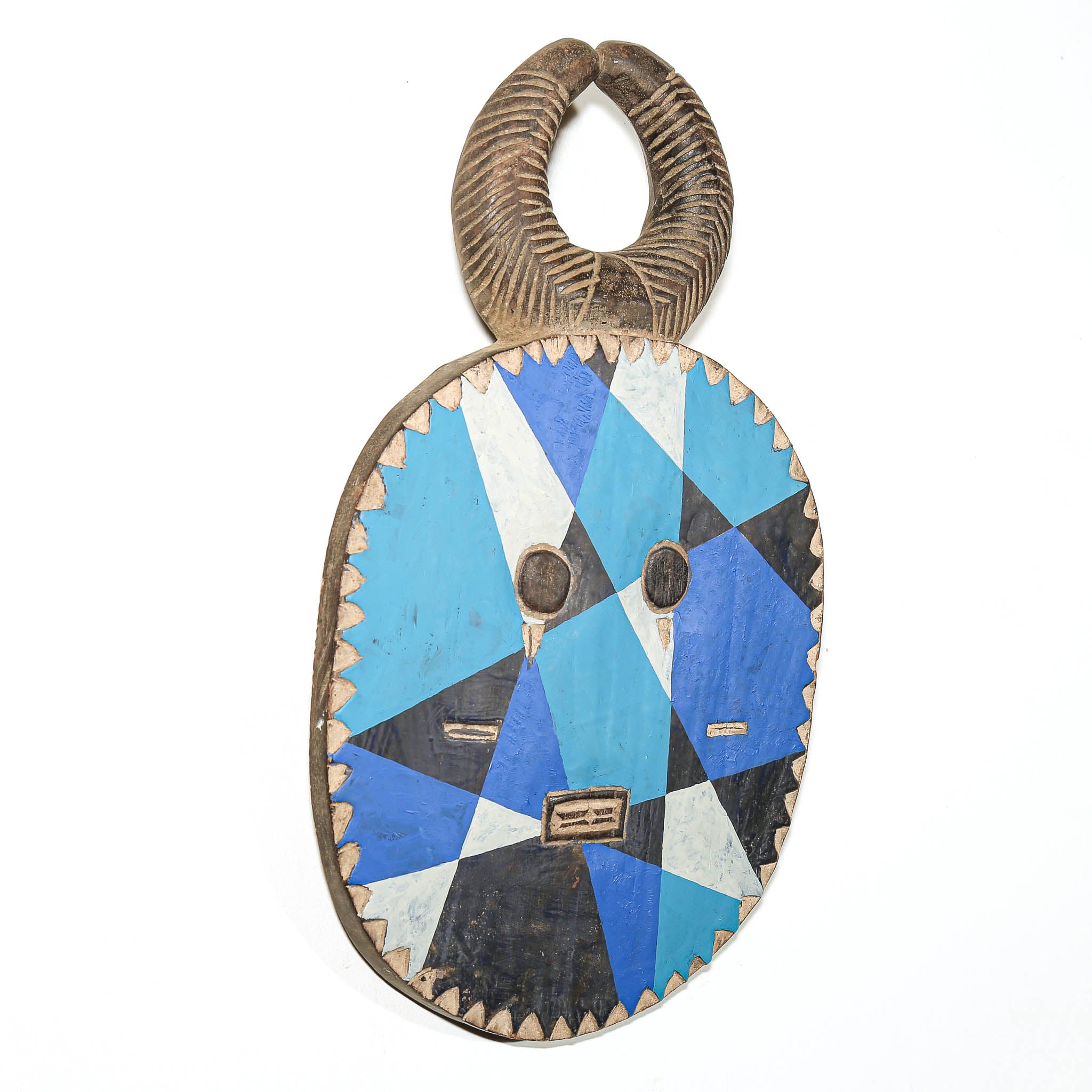A hand-carved African wooden mask with a geometric blue, black, and white pattern, featuring a textured handle on top, photographed against a plain white background.
