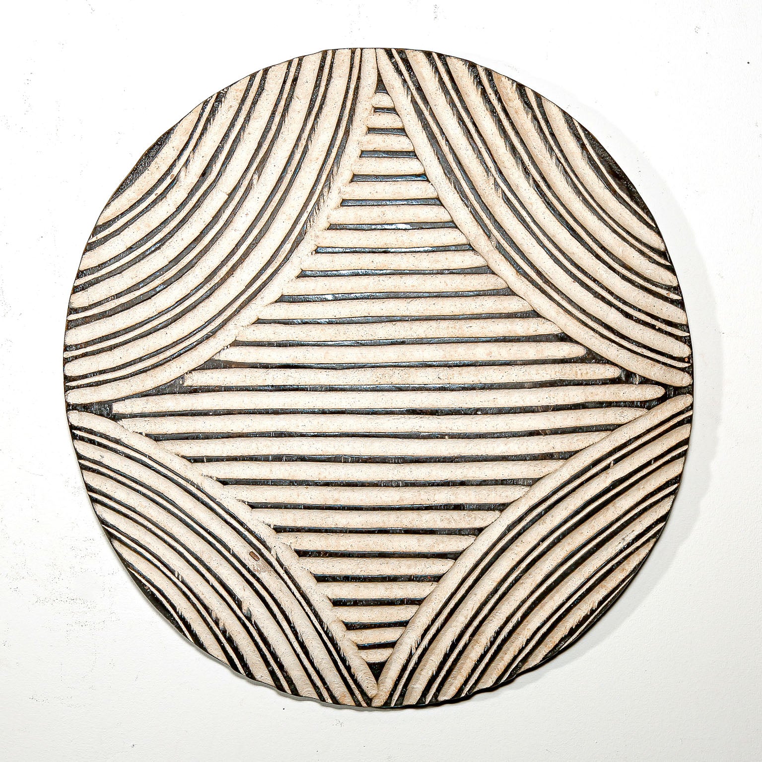 Round wood wall decor with rustic African traditional striped pattern on a white living room wall
