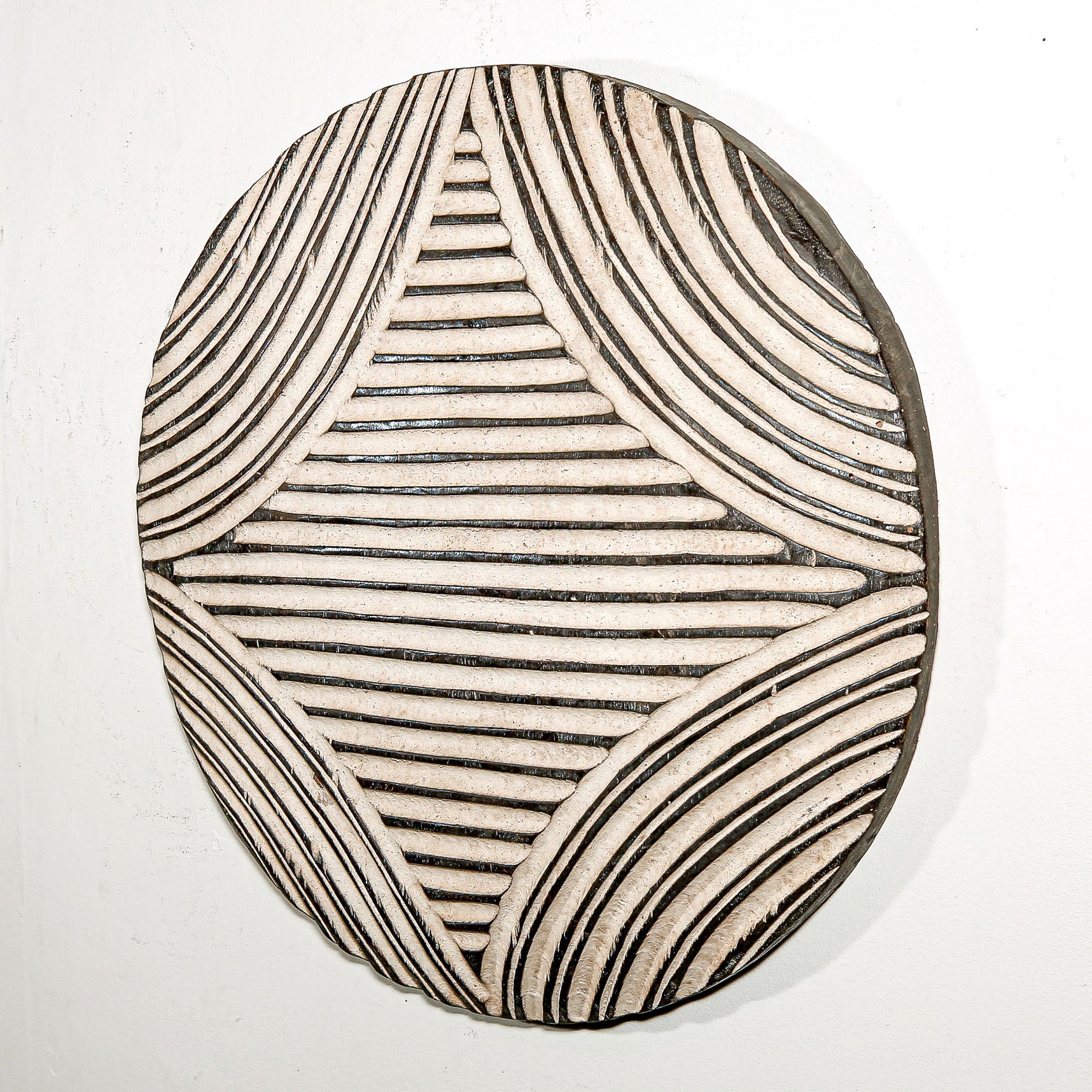 Round wood wall decor with rustic African traditional striped pattern on a white living room wall