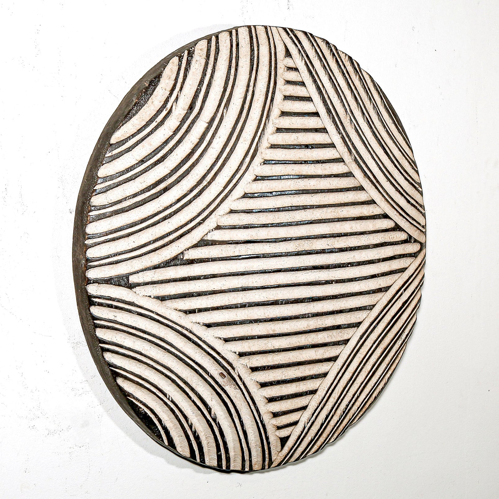 Round wood wall decor with rustic African traditional striped pattern on a white living room wall