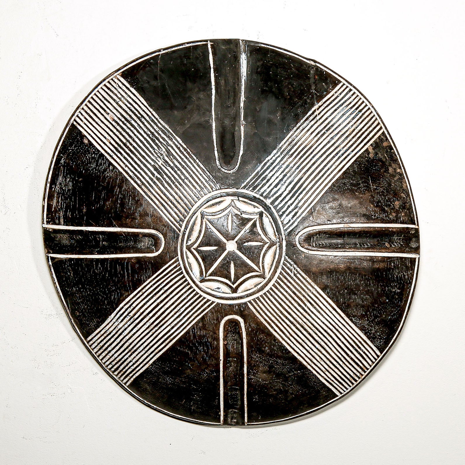 Round wood wall decor with rustic African traditional star pattern on a white living room wall