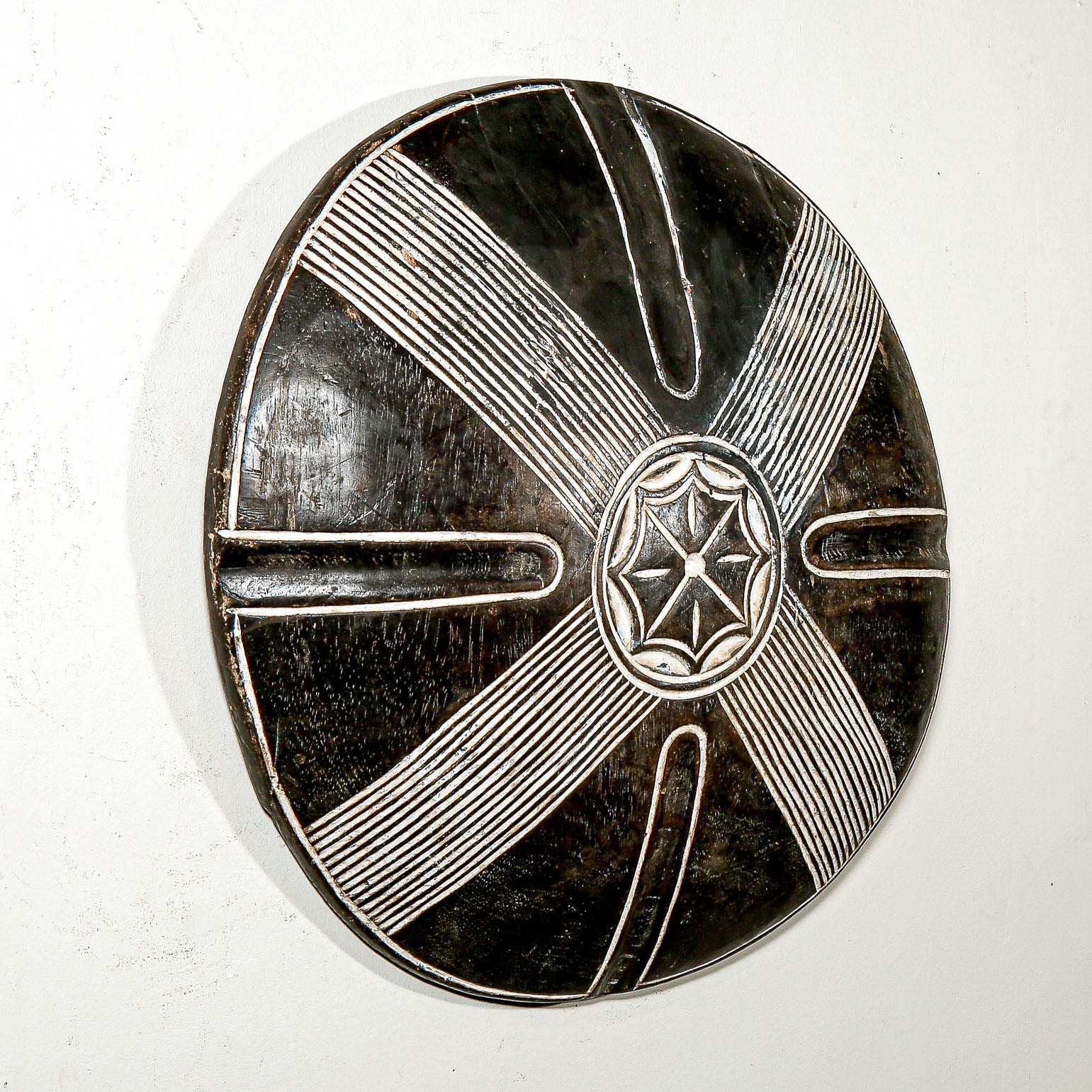 Round wood wall decor with rustic African traditional star pattern on a white living room wall