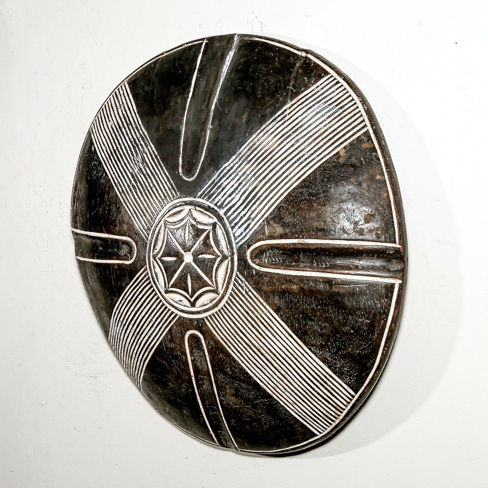 Round wood wall decor with rustic African traditional star pattern on a white living room wall