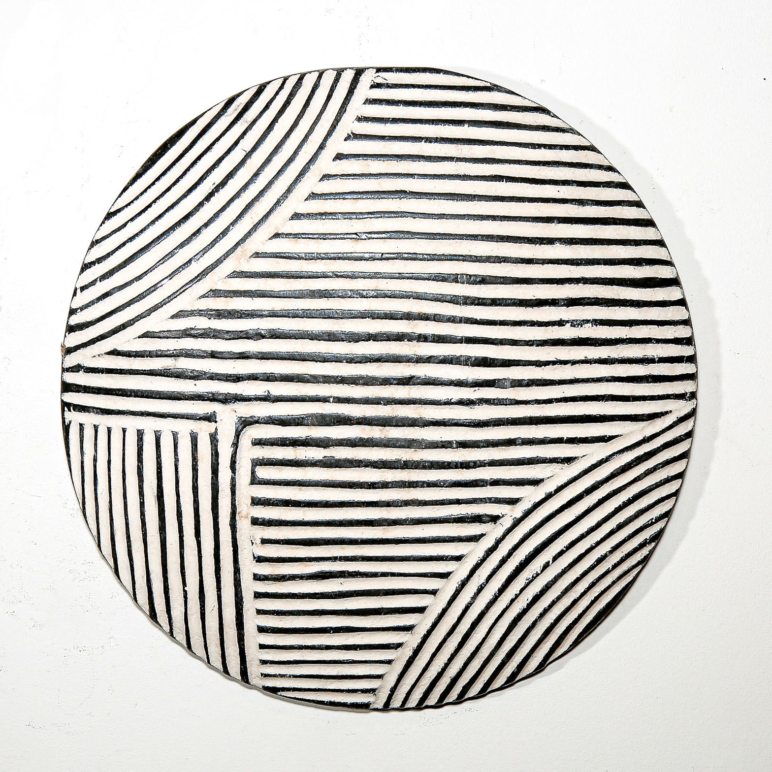 Round wood wall decor with rustic African traditional striped pattern on a white living room wall