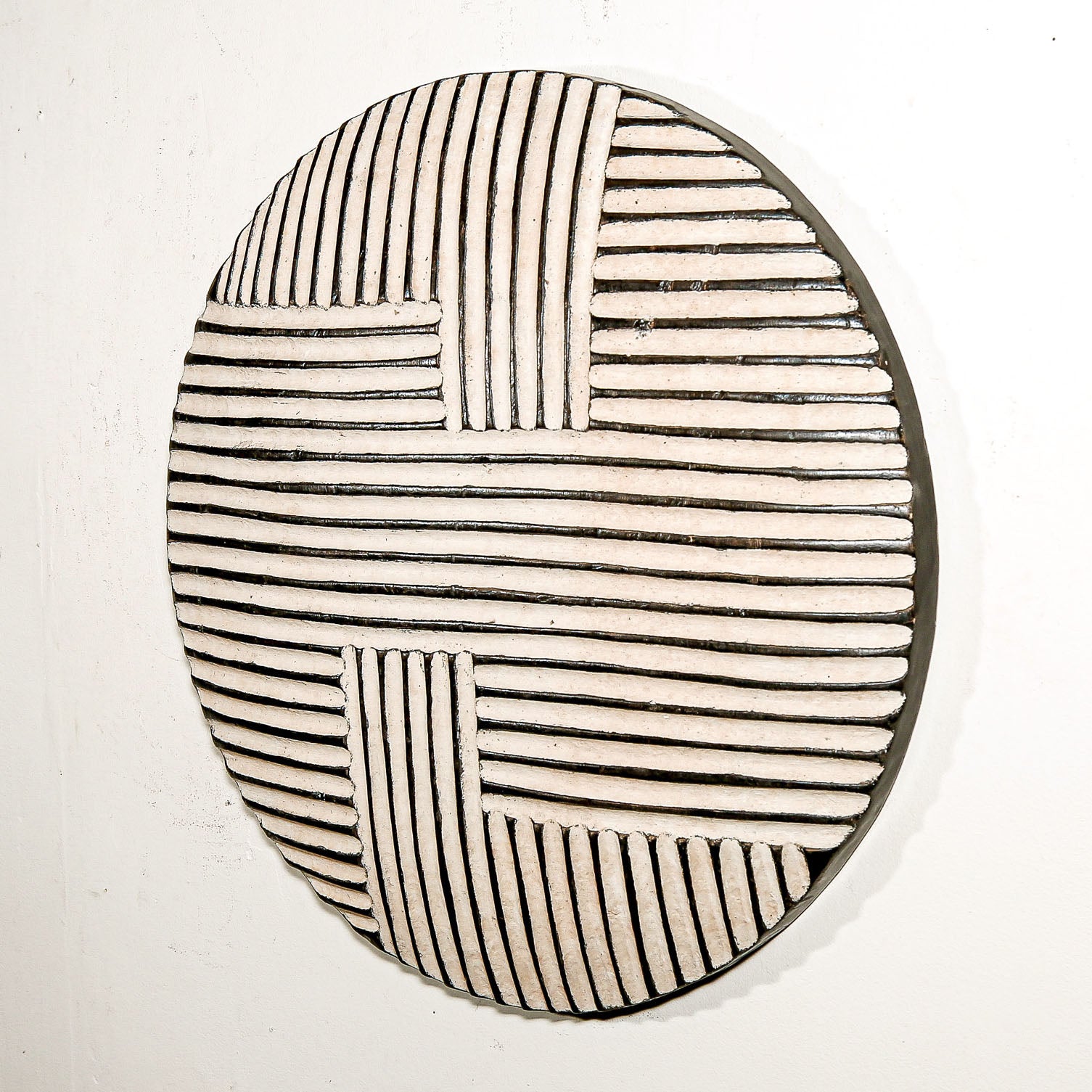 Round wood wall decor with rustic African traditional striped pattern on a white living room wall