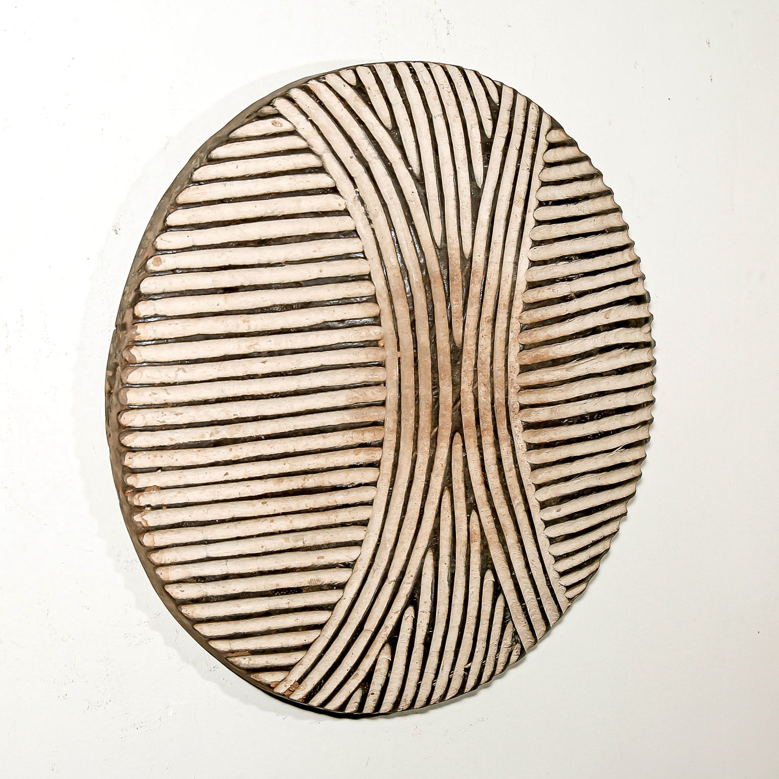 Round wood wall decor with rustic African traditional striped pattern on a white living room wall