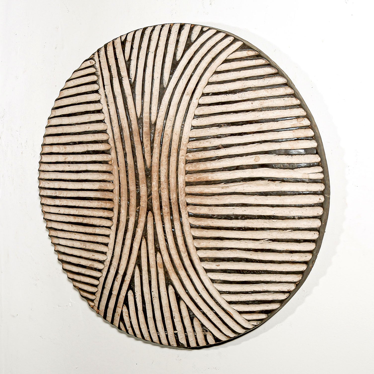 Round wood wall decor with rustic African traditional striped pattern on a white living room wall