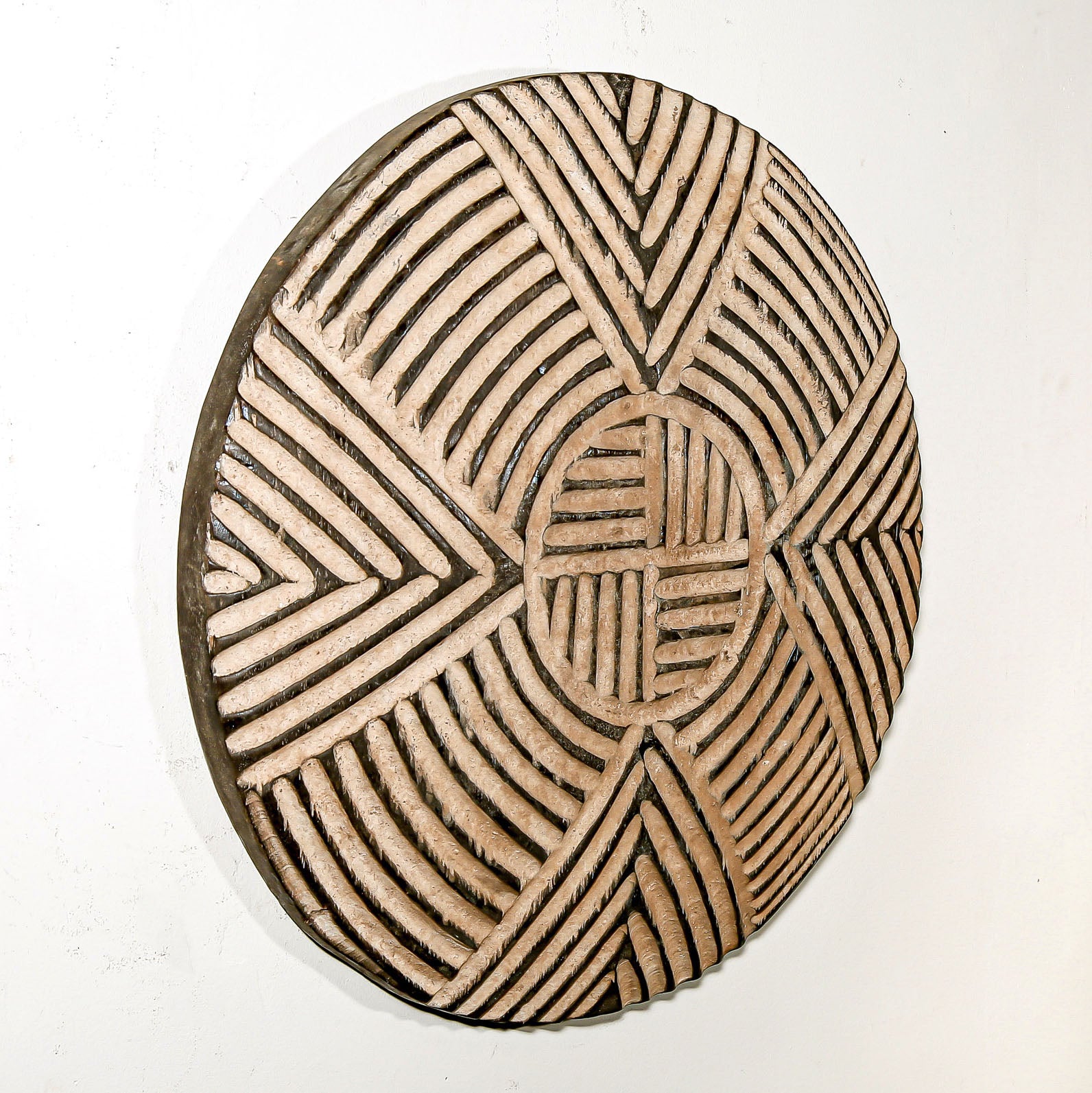 Round wood wall decor with rustic African traditional striped pattern on a white living room wall