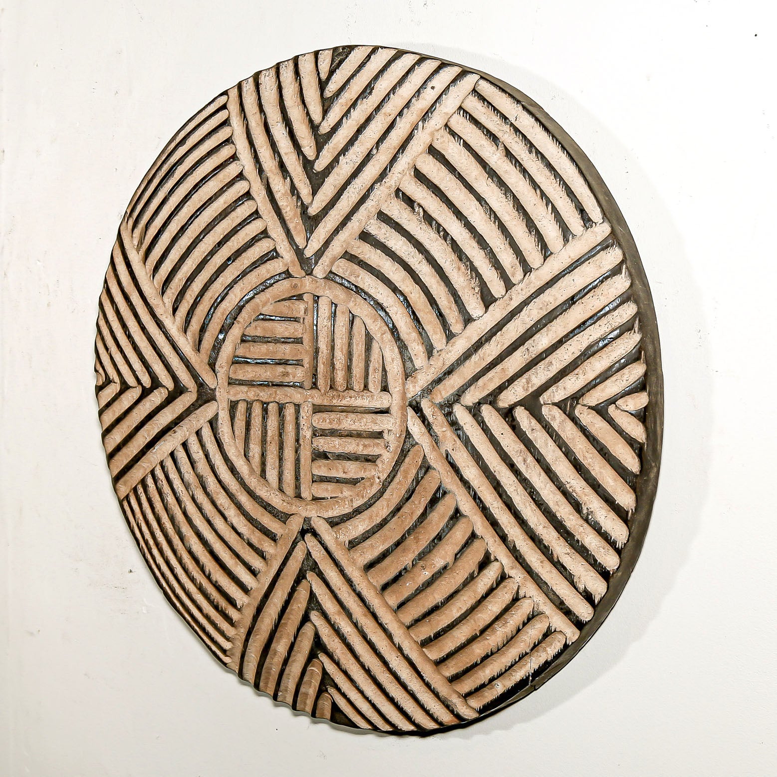 Round wood wall decor with rustic African traditional striped pattern on a white living room wall