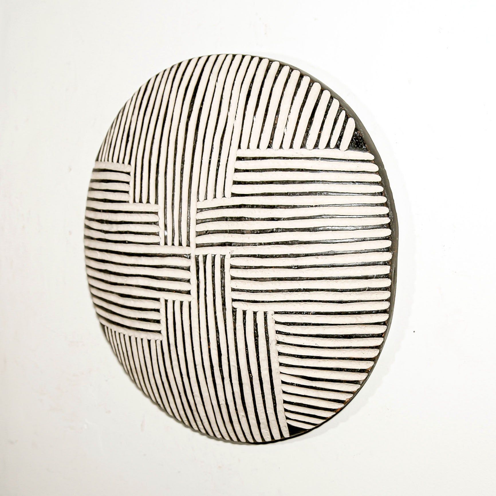 Round wood wall decor with rustic African traditional striped pattern on a white living room wall