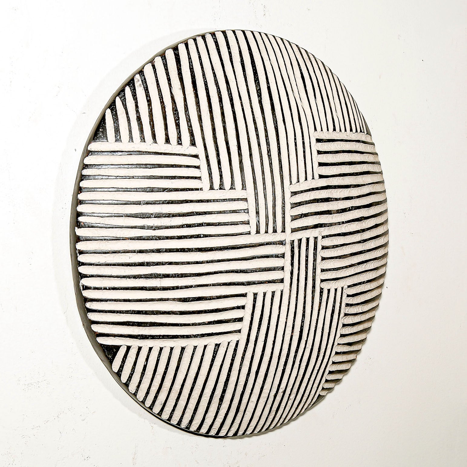 Round wood wall decor with rustic African traditional striped pattern on a white living room wall