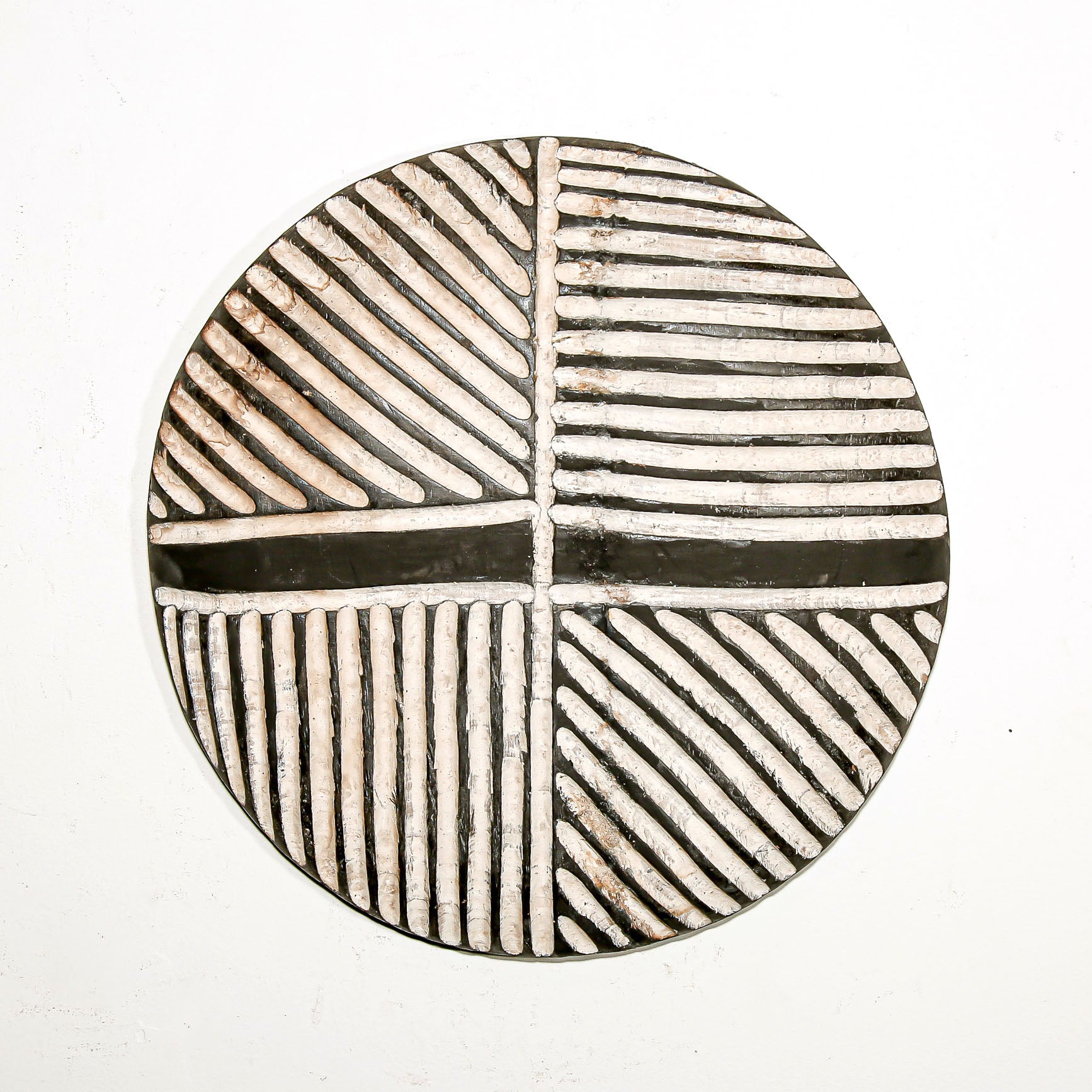 Round wood wall decor with rustic African traditional striped pattern on a white living room wall