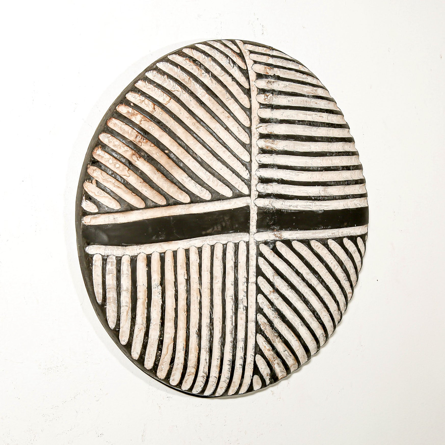 Round wood wall decor with rustic African traditional striped pattern on a white living room wall
