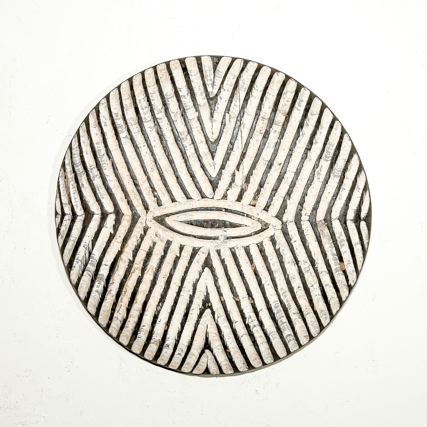 Round wood wall decor with rustic African traditional striped pattern on a white living room wall