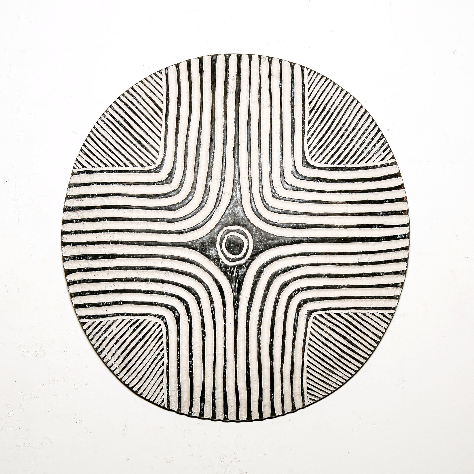 Round wood wall decor with rustic African traditional striped pattern on a white living room wall