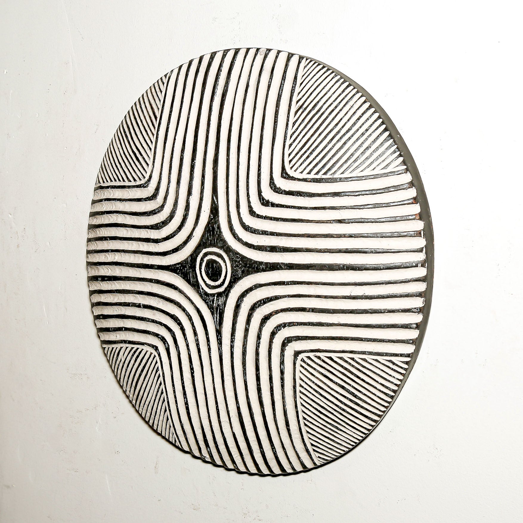 Round wood wall decor with rustic African traditional striped pattern on a white living room wall