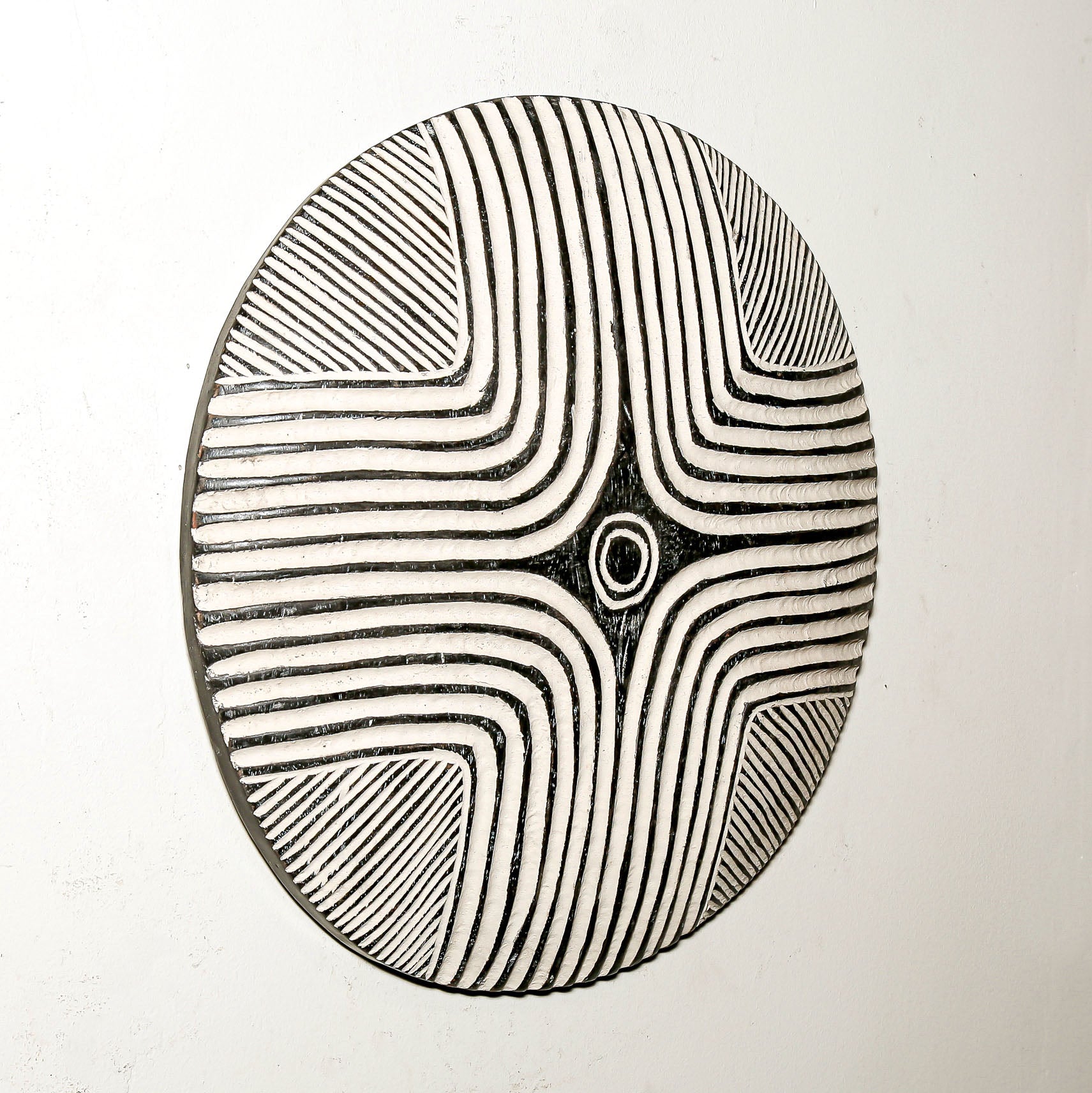 Round wood wall decor with rustic African traditional striped pattern on a white living room wall